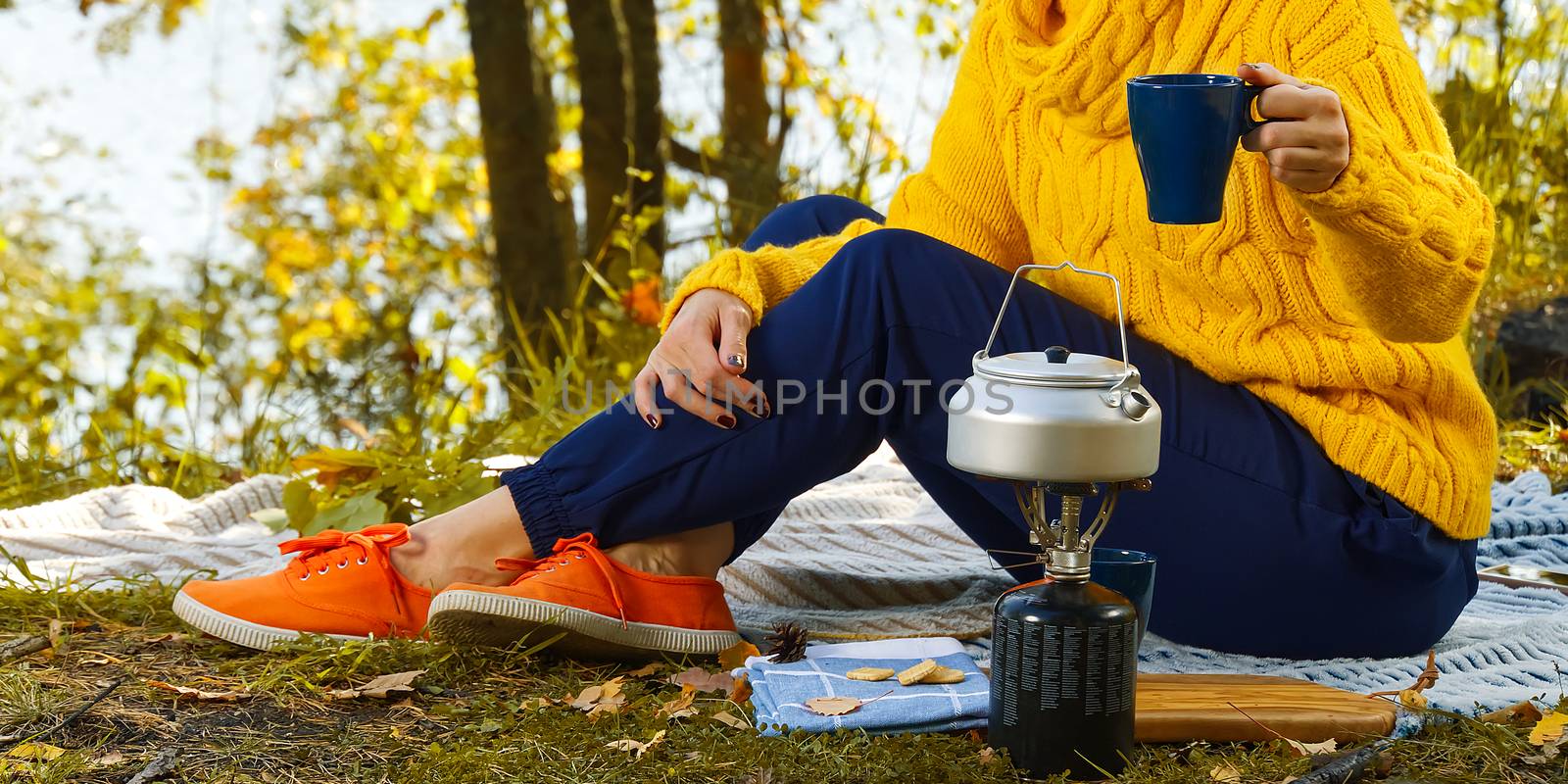 young beautiful girl in a yellow sweater makes coffee in the forest on a gas burner. Making coffee on a primus stove in the autumn forest, step by step. Camping in autumn forest concept