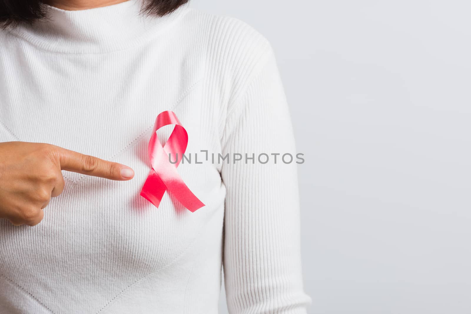 Breast cancer awareness healthcare and medicine concept. Close up Asian woman wear white shirt pointing finger to pink breast cancer awareness ribbon, studio shot isolated on white background