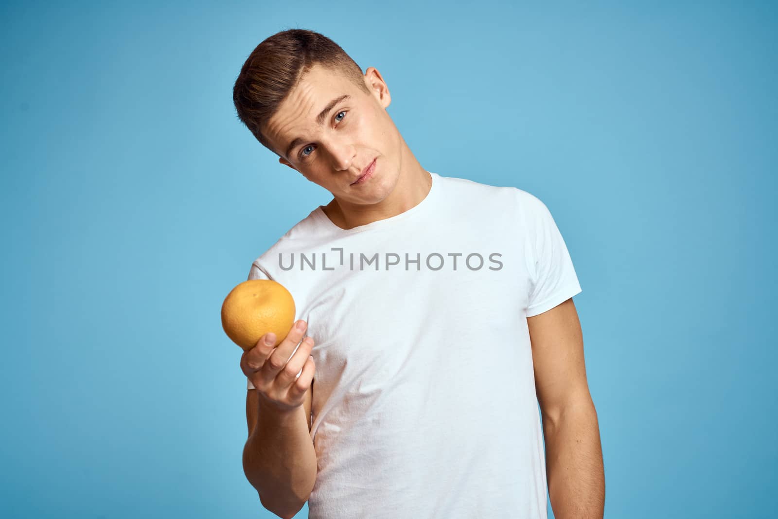 Happy man with fresh fruits gesturing with hands blue background white t-shirt vitamins oranges by SHOTPRIME