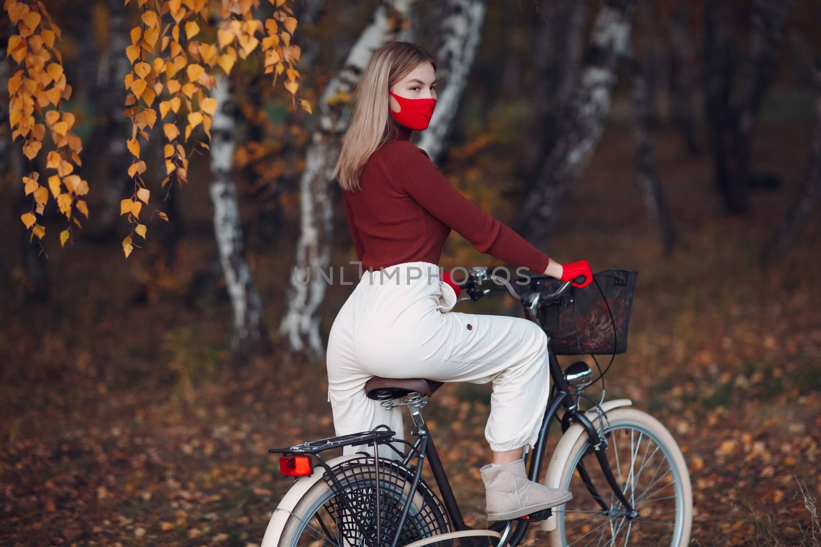 Young woman riding bicycle in red gloves and face mask at autumn park by primipil