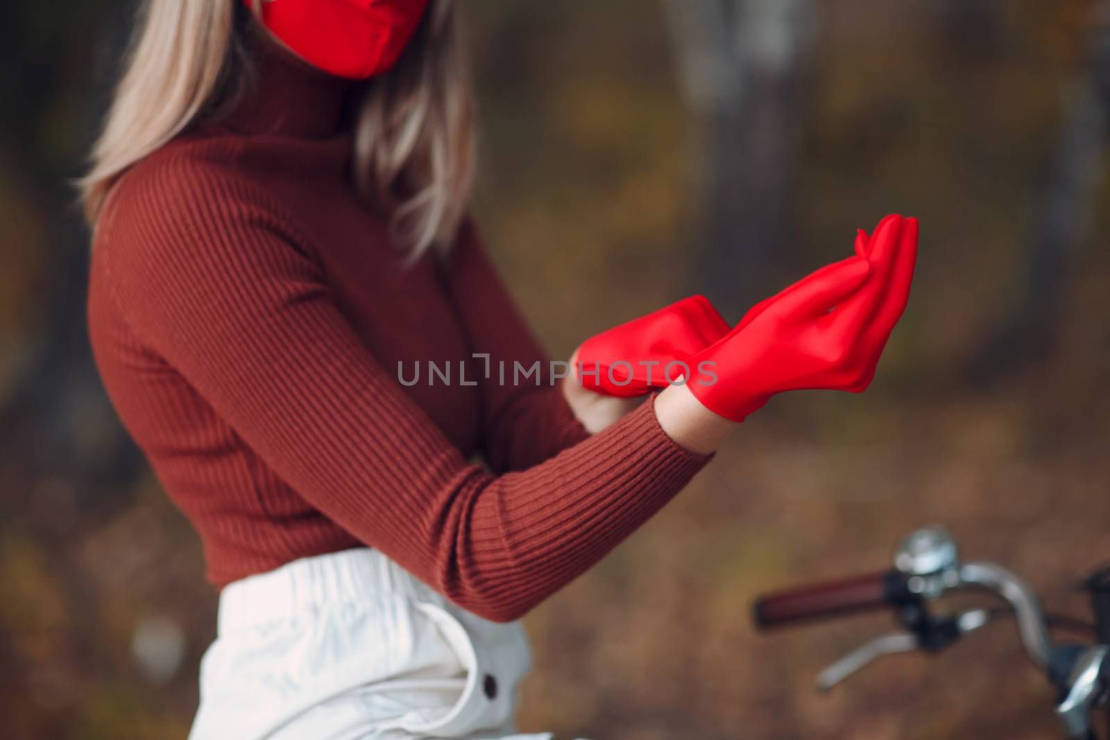 Young woman riding bicycle and put on red gloves and face mask at autumn park by primipil