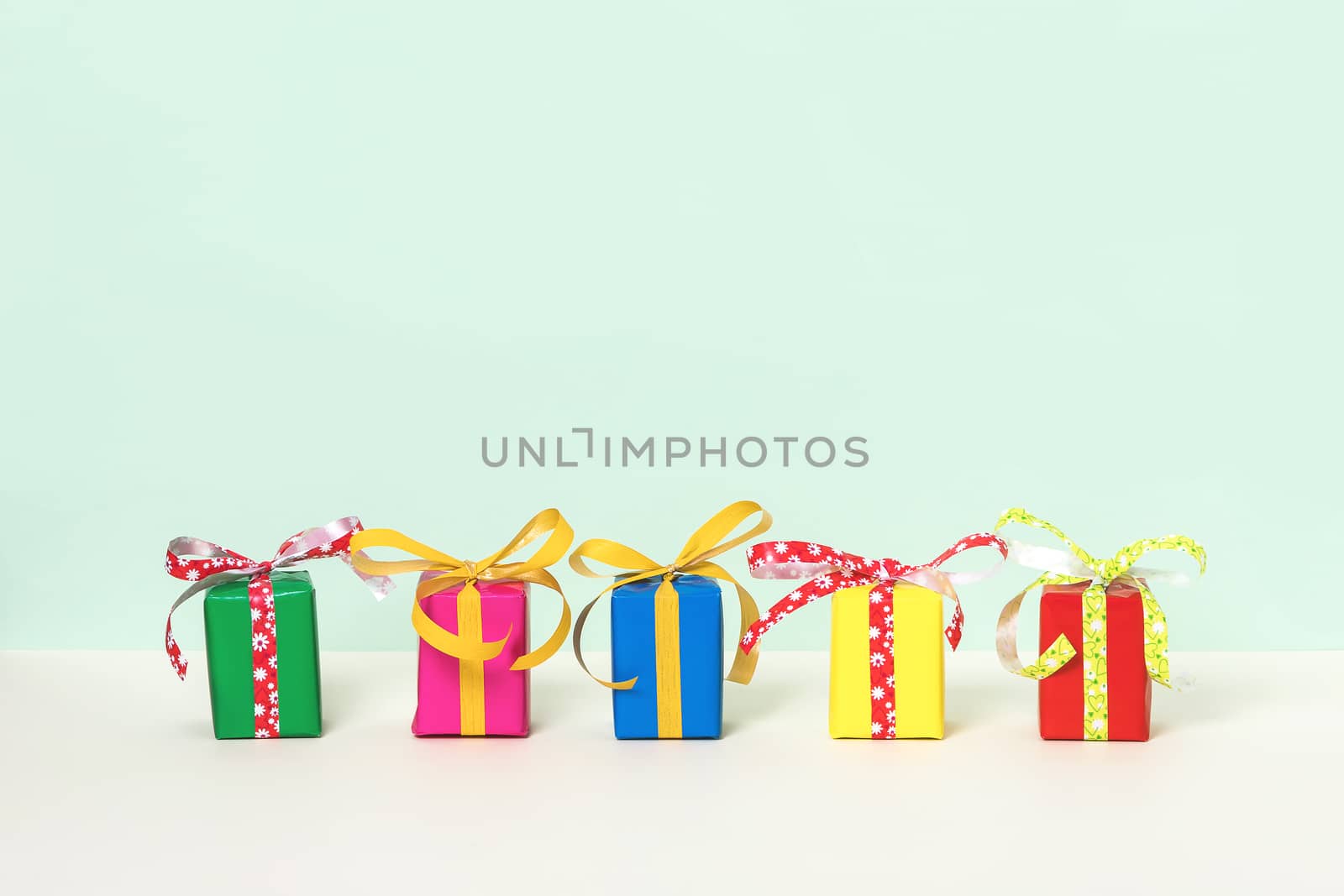 Row with five colorful gift boxes on a pastel background. Copy space. Front view.