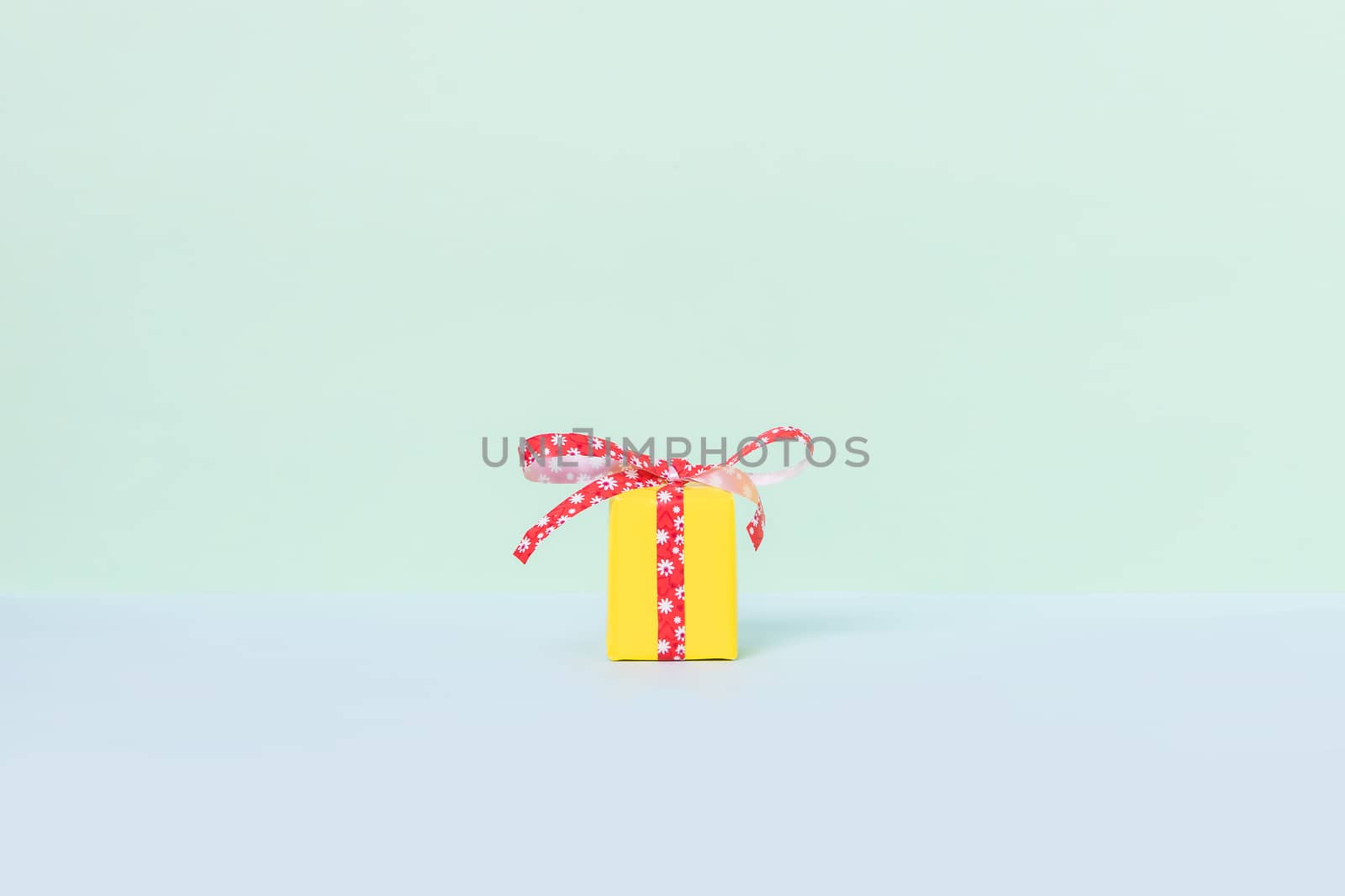 Yellow gift box with red ribbon on a pastel background. Copy space. Front view.