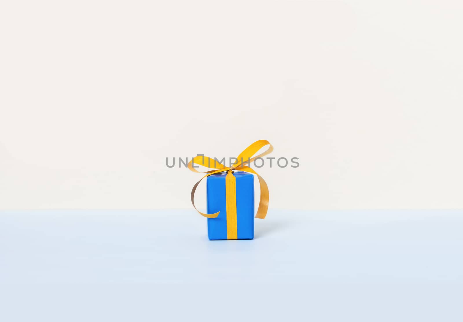 Blue gift box with yellow ribbon on a pastel background. Copy space. Front view.