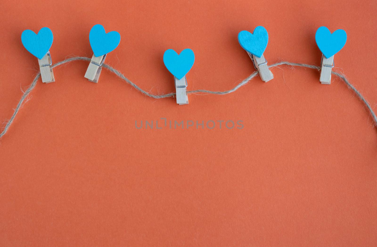 Small clothespins and blue hearts on a rope on an orange background.