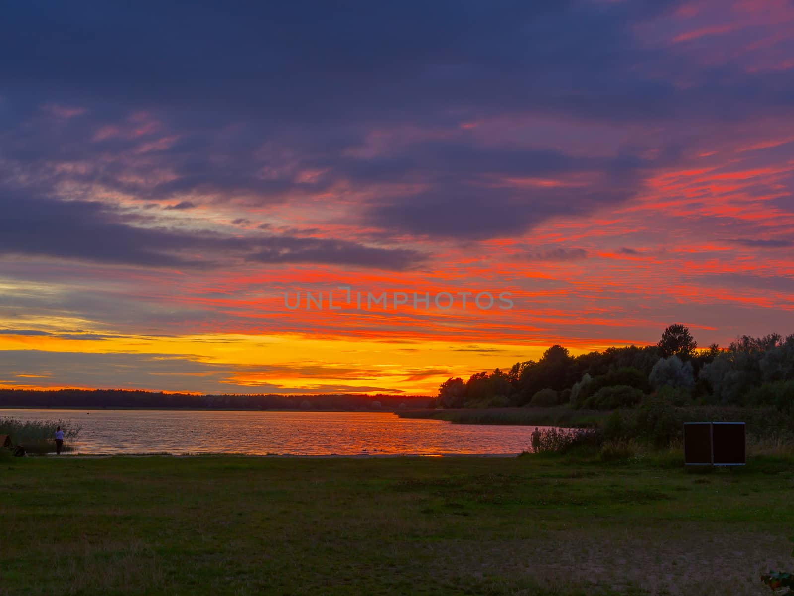 Panoramic view of evening sunset lake with green trees, mist and tranquil reflection. Estonia, Harku. Sunset over lake