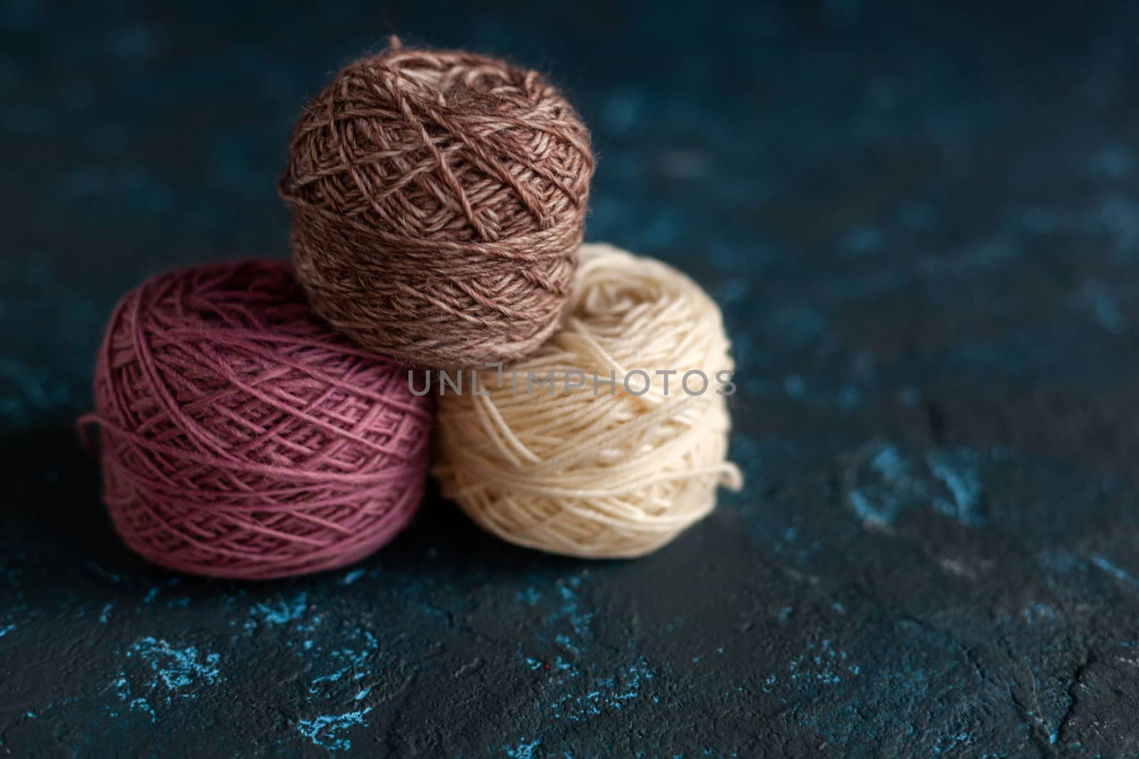 three beige pink brown Color balls skein of wool yarn for crochet and knit on dark blue texture putty concrete. Flatlay image with space for text.
