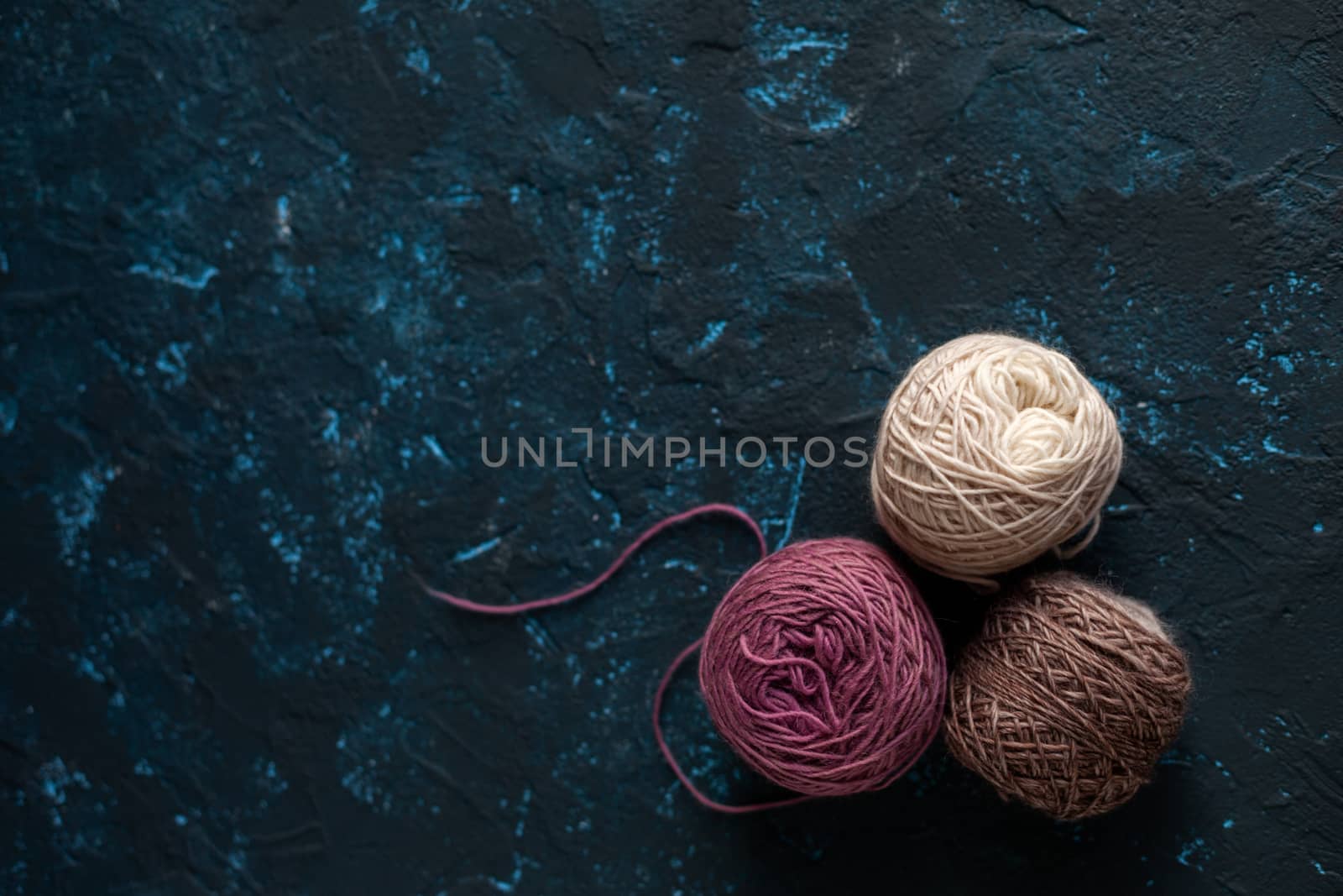 three beige pink brown Color balls skein of wool yarn for crochet and knit on dark blue texture putty concrete. Flatlay image with space for text.
