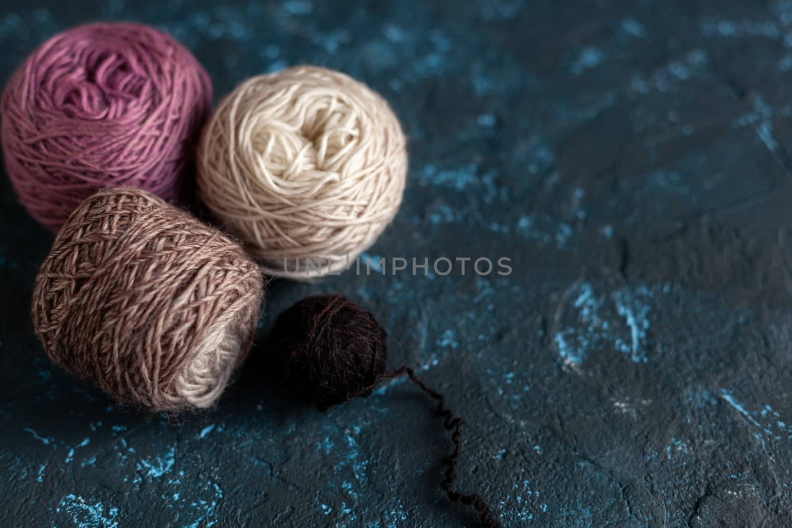 Four beige pink brown Color balls skein of wool yarn for crochet and knit on dark blue texture putty concrete. Flatlay image with space for text.