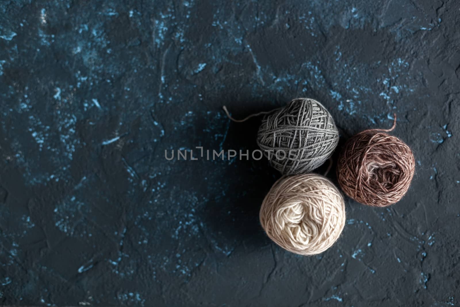 three beige gray brown Color balls skein of wool yarn for crochet and knit on dark blue texture putty concrete. Flatlay image with space for text.