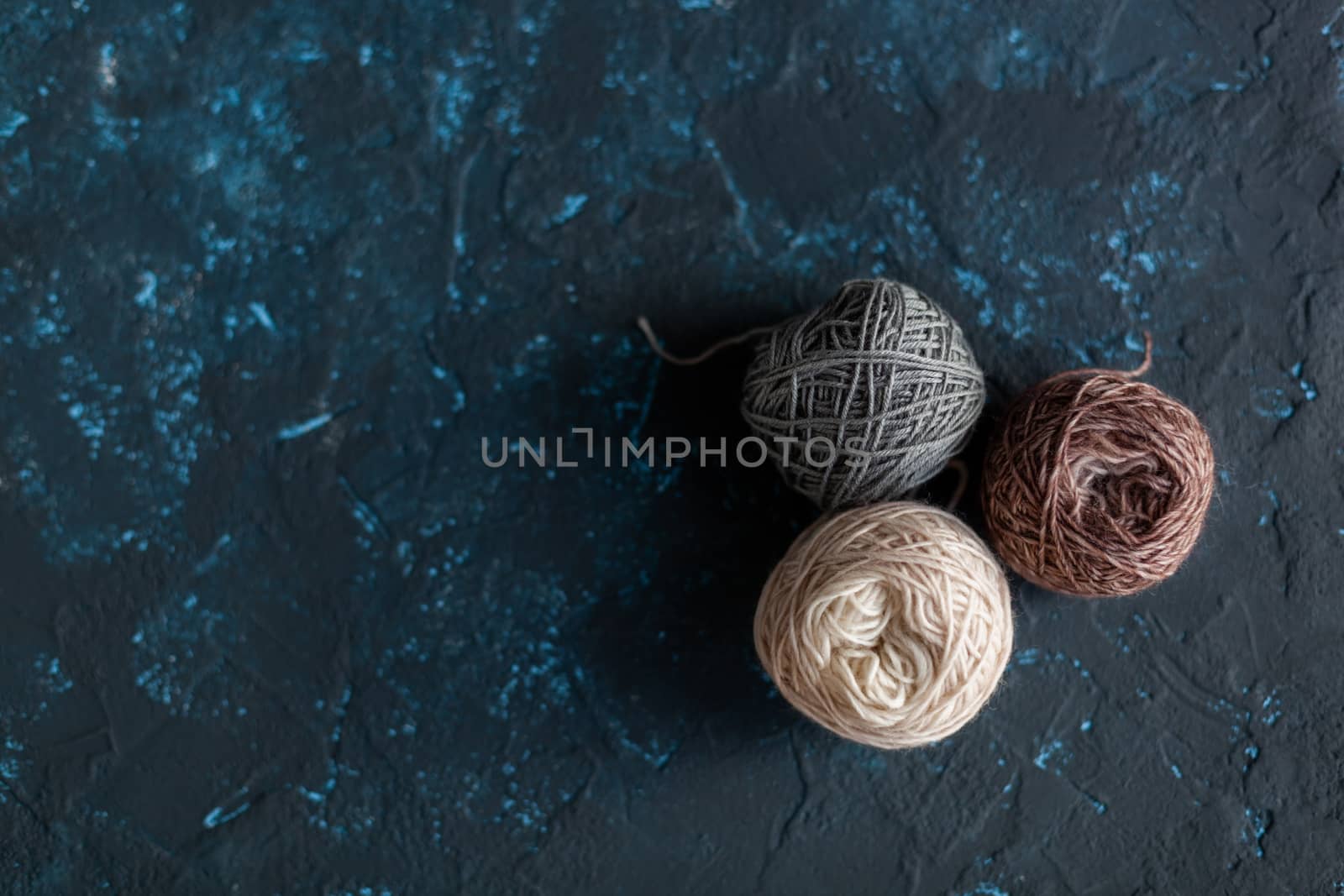 three beige gray brown Color balls skein of wool yarn for crochet and knit on dark blue texture putty concrete. Flatlay image with space for text.