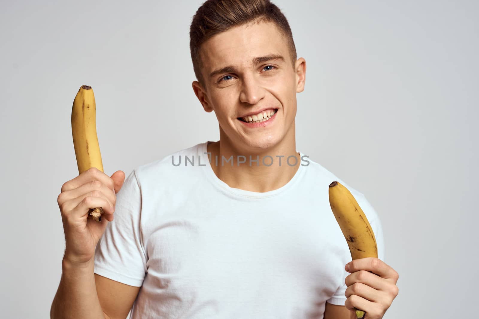 guy with a banana in his hand on a light background fun emotions light background white t-shirt model by SHOTPRIME