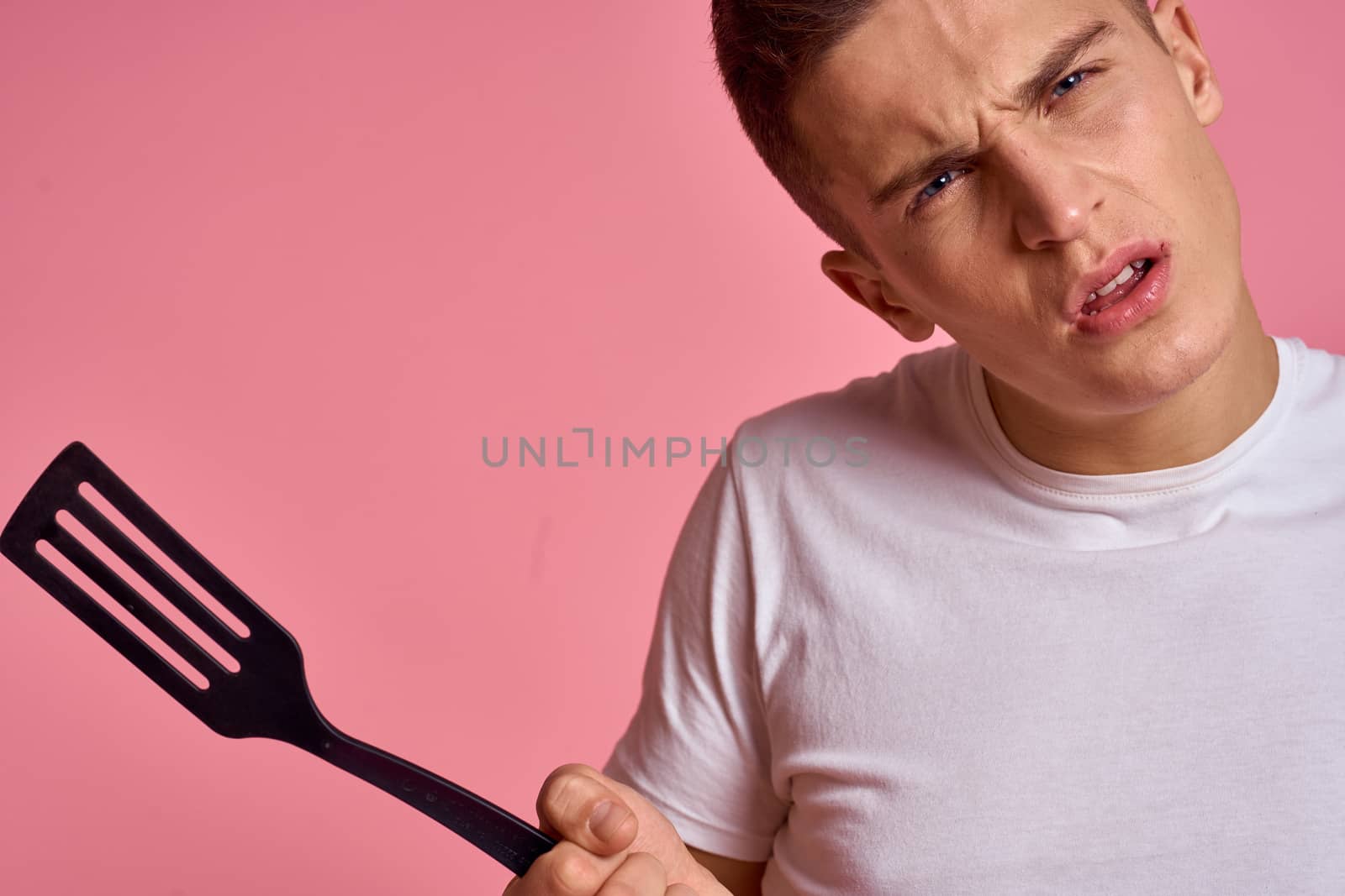 Man with kitchen tools on pink background spatula for cooking model cropped view. High quality photo