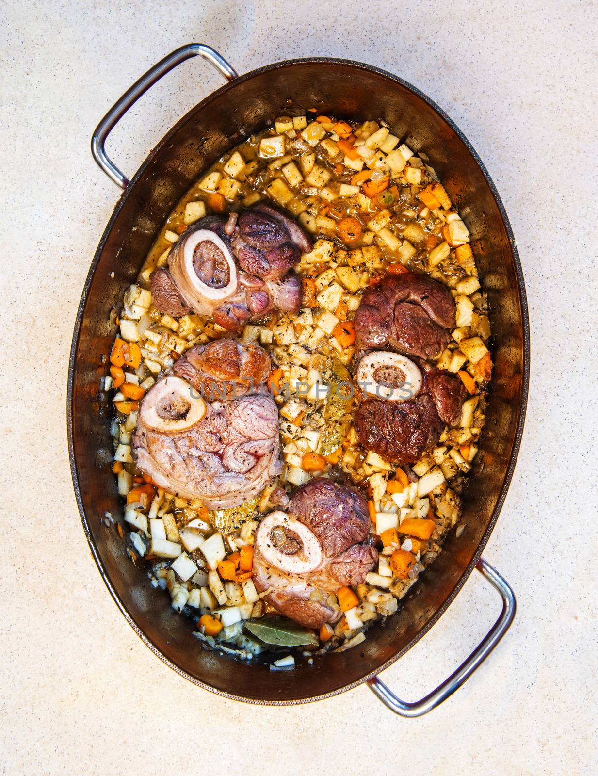 Osso buco in bianco is traditional Italain dish from the Milan area. The veal meat slices with marrow bone are being cooked in a large casserole along with root vegetables, spice and wine sauce