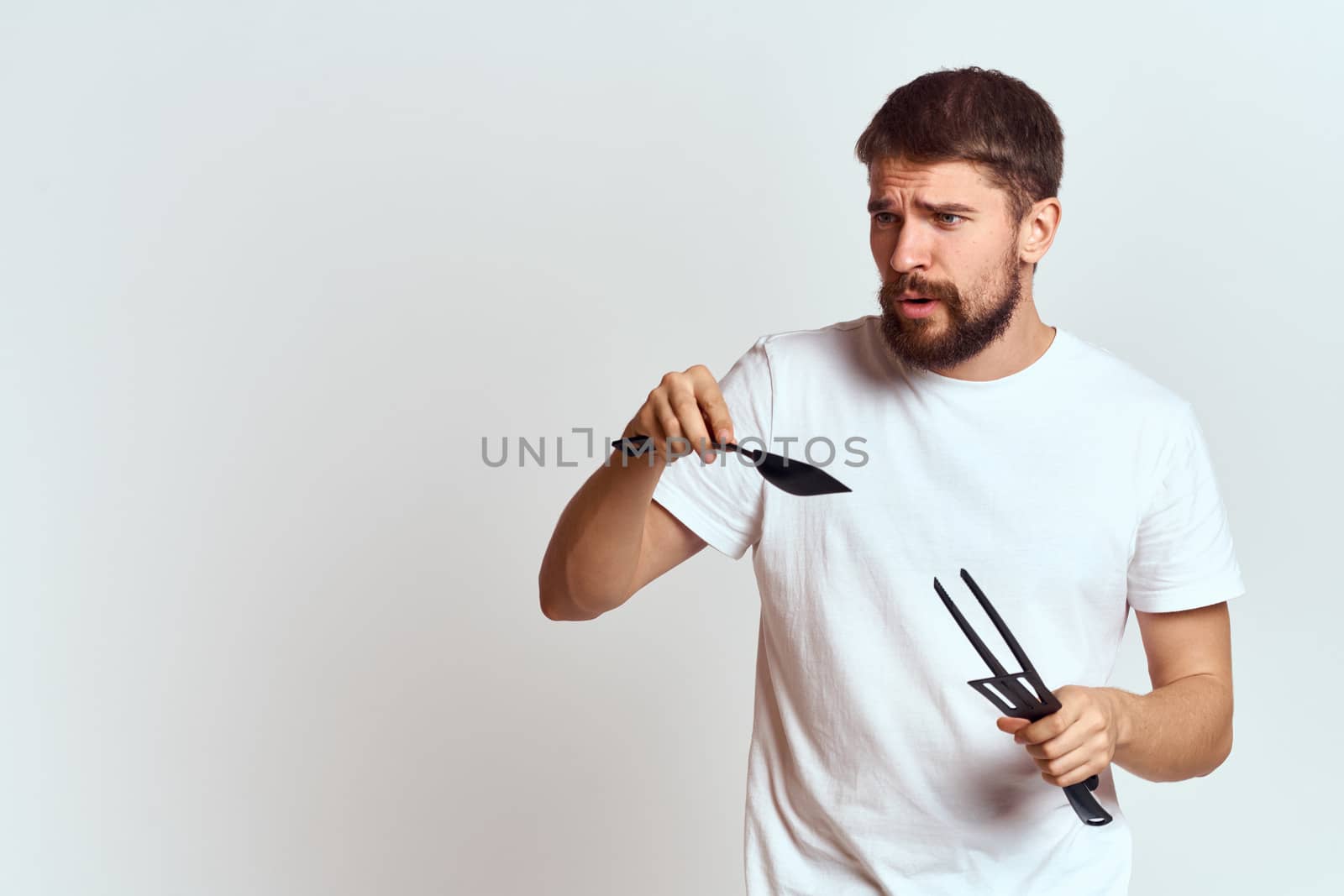 A man with kitchen appliances in the hands of their white T-shirt on a light background cropped view by SHOTPRIME