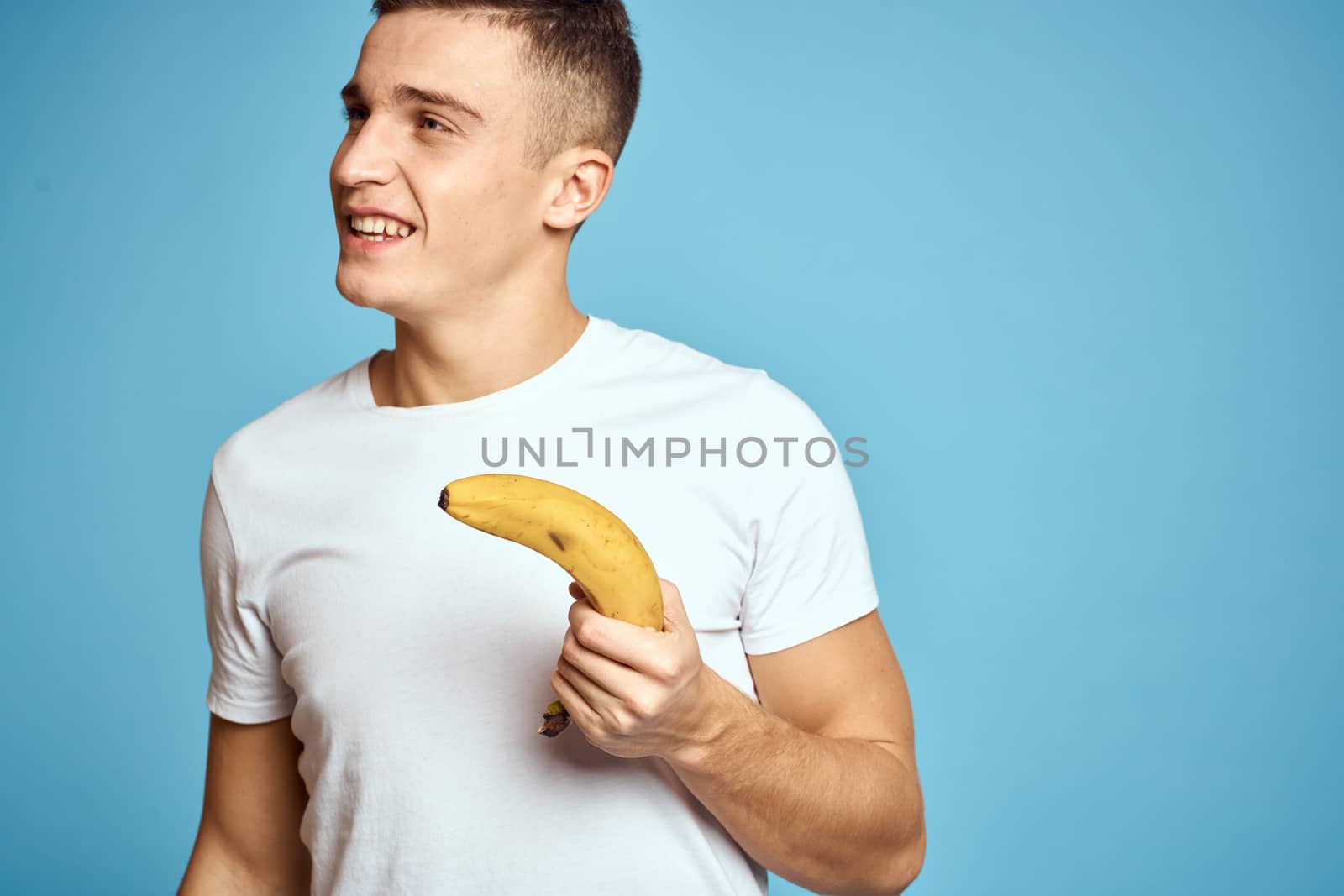 Happy man with fresh fruits gesturing with hands blue background white t-shirt vitamins bananas by SHOTPRIME