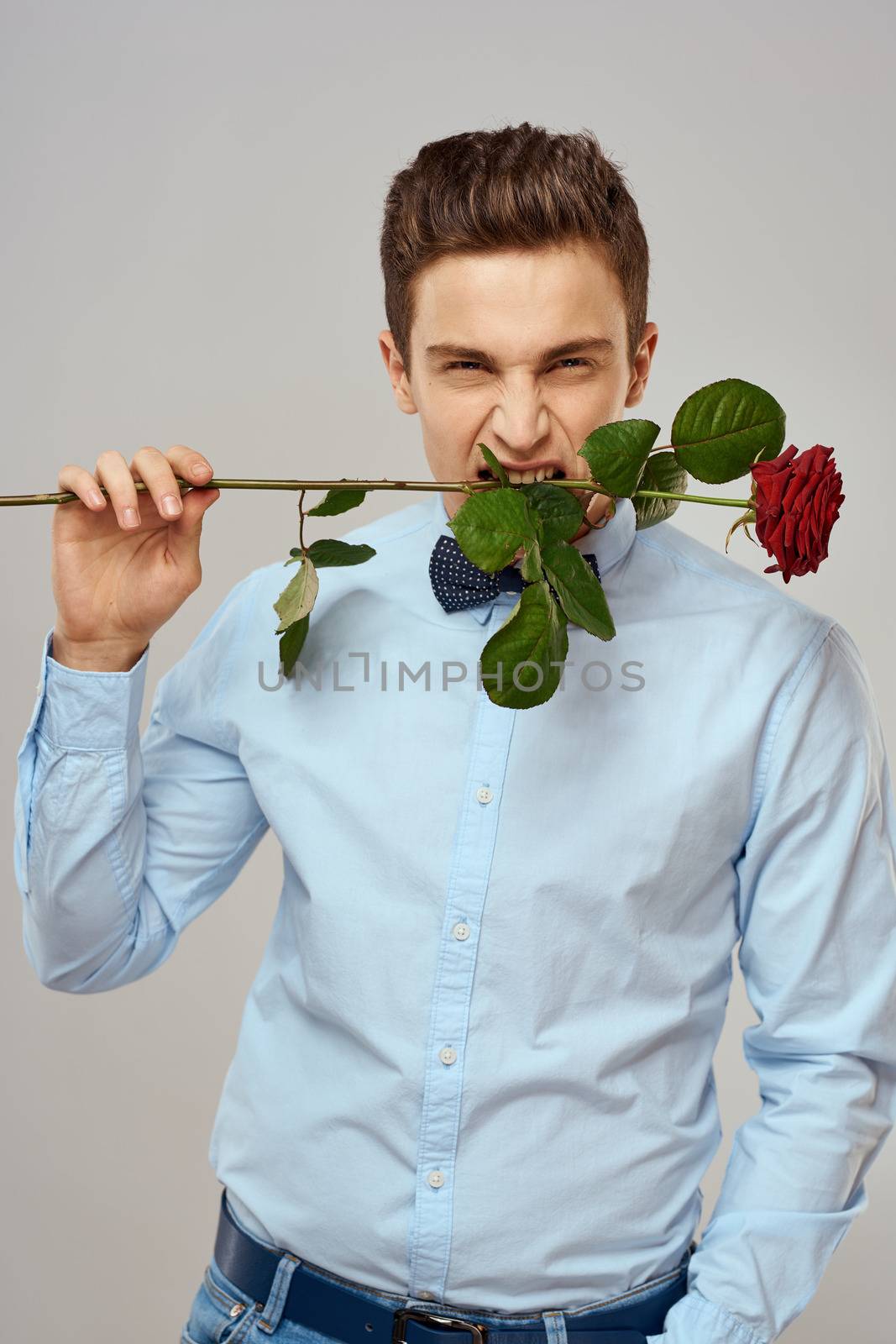 Romantic man with a red rose and in a blue shirt with a bow tie around his neck gray background by SHOTPRIME