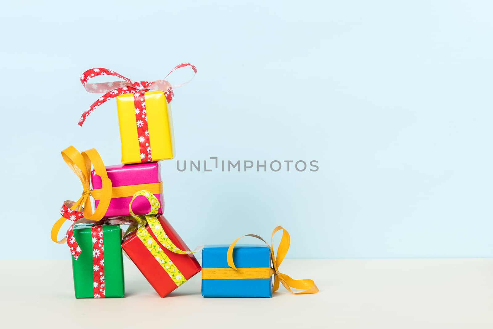 Five colorful gift boxes stacked on a pastel background with space for your text. Front view.