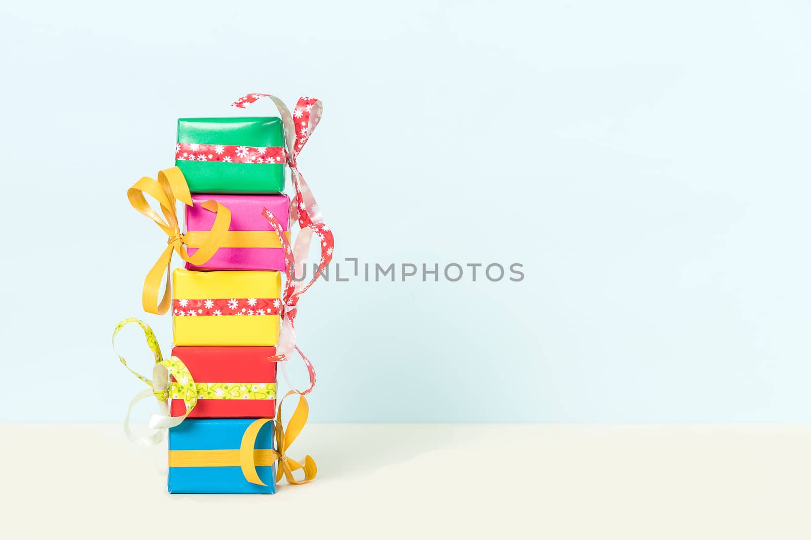 Five colorful gift boxes stacked on a pastel background with space for your text. Front view.