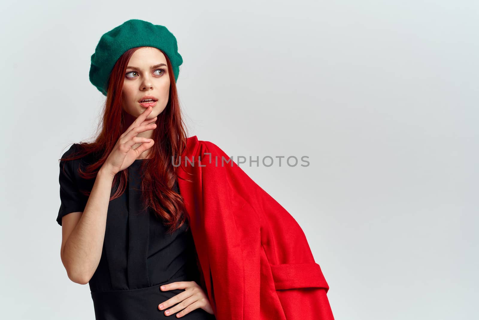 A woman holds in her hand a red coat and a dark T-shirt Green hat cropped view of a light background by SHOTPRIME