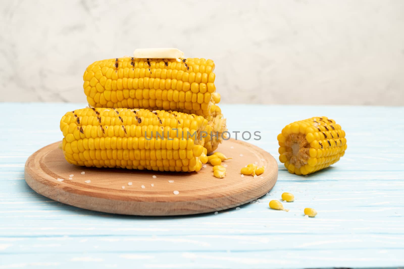 Grilled hot Corn cob lies on round cutting board plate blue wooden table background. Copy space for text.