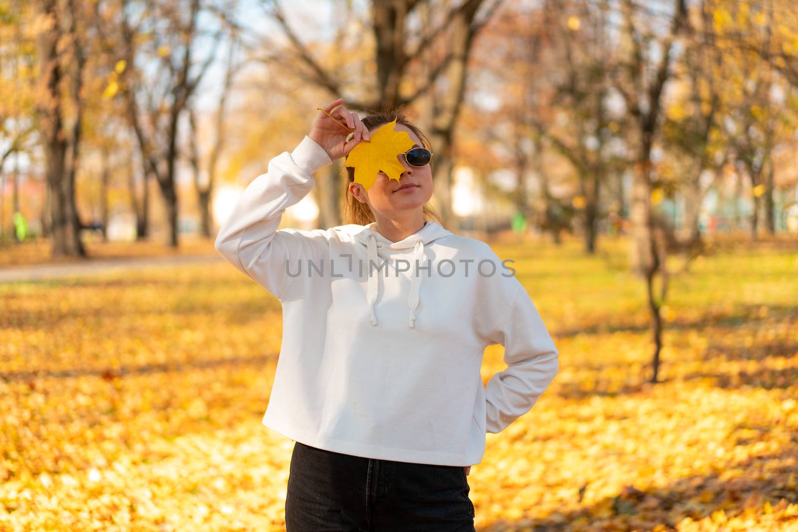 Portrait of beautiful young woman in a white sweater and sunglasses walking outdoors in autumn. White hoodie