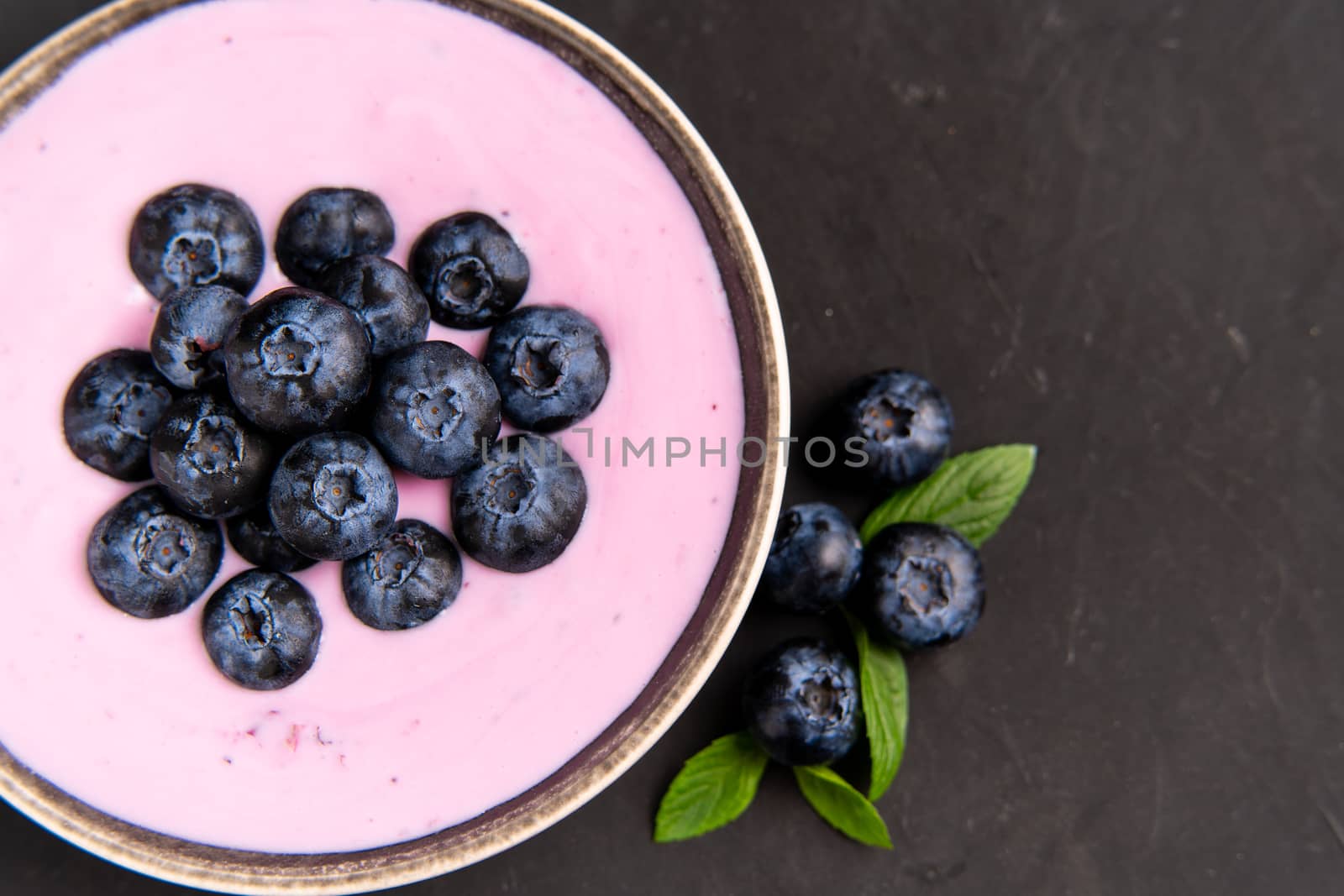 Tasty fresh blueberry yoghurt shake dessert in ceramic bowl standing on black table background. Homemade berry smoothie. Healthy eating. Diet food. yogurt