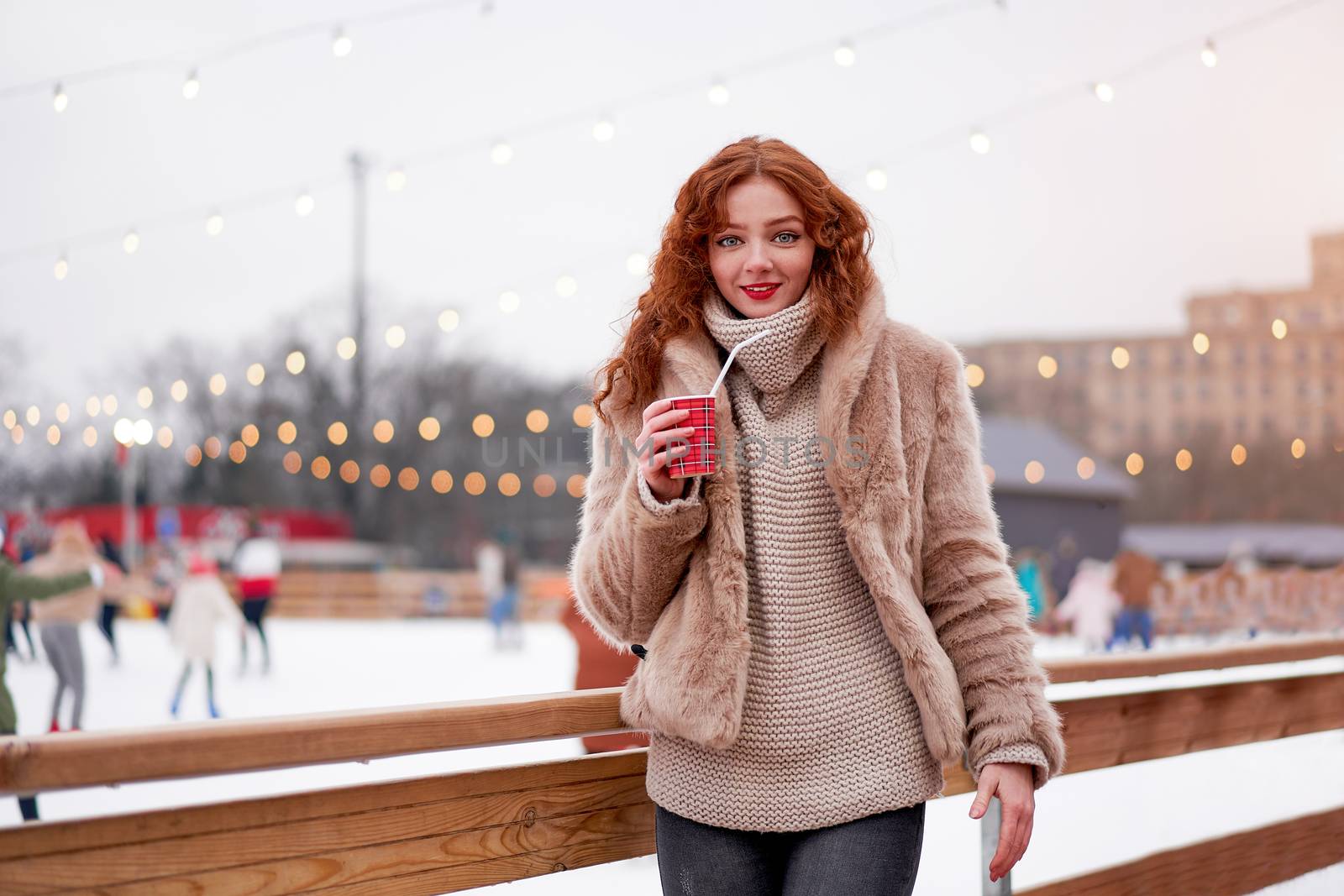 Young beautiful redhead girl freckles ice rink background Pretty woman curly hair portrait walking new year fair Modern cute female skate ice rink chrismas holiday decorated street.