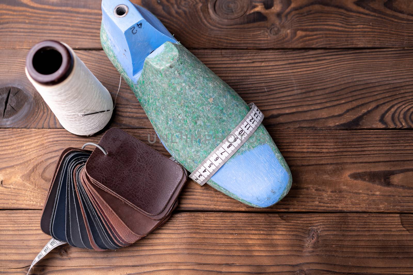 Leather samples for shoes and wooden shoe last on dark wooden table. Designer furniture clothes. Shoe maker workspace.