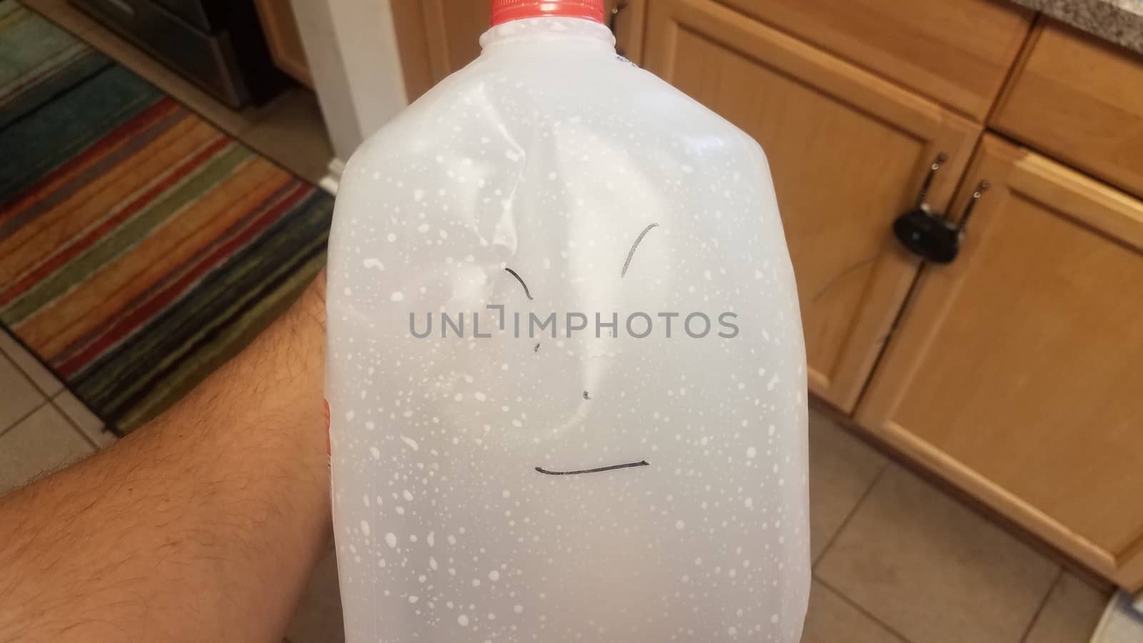 angry face drawn on empty milk gallon jug in kitchen