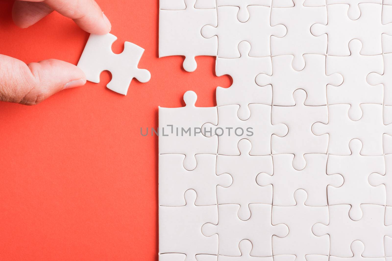 Top view flat lay of hand-holding last piece white paper jigsaw puzzle game last pieces put to place for solve problem complete mission, studio shot on a pink background, quiz calculation concept