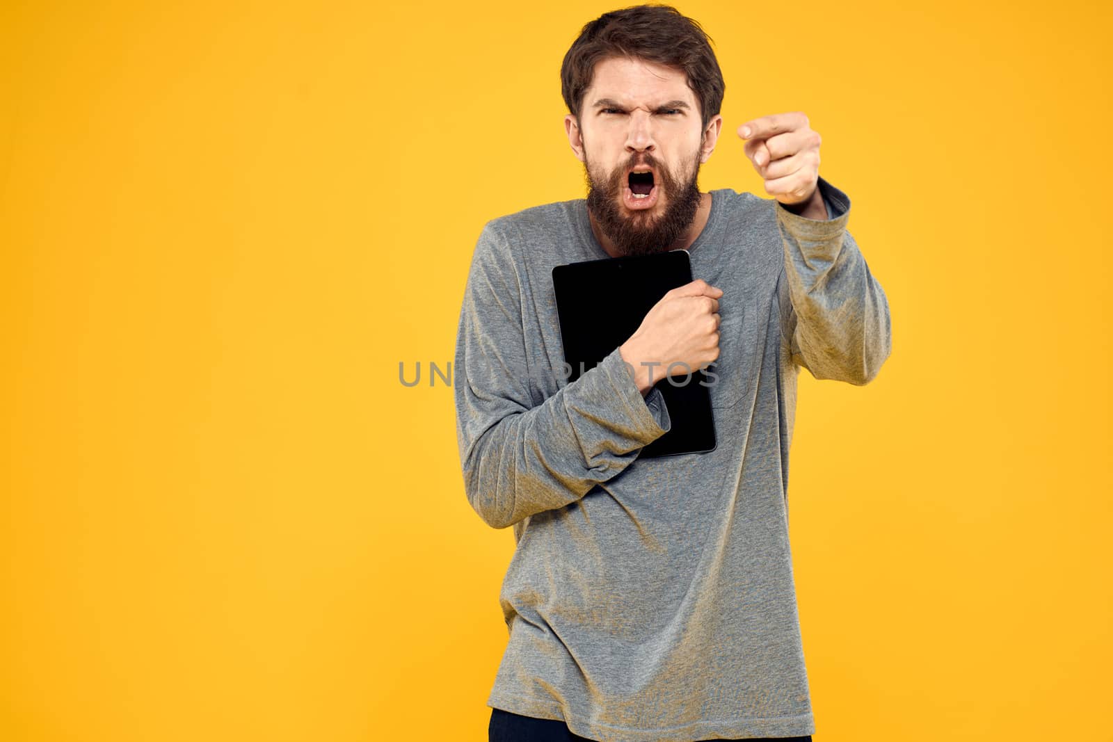 Emotional man with tablet in hands technology internet device lifestyle yellow background. High quality photo