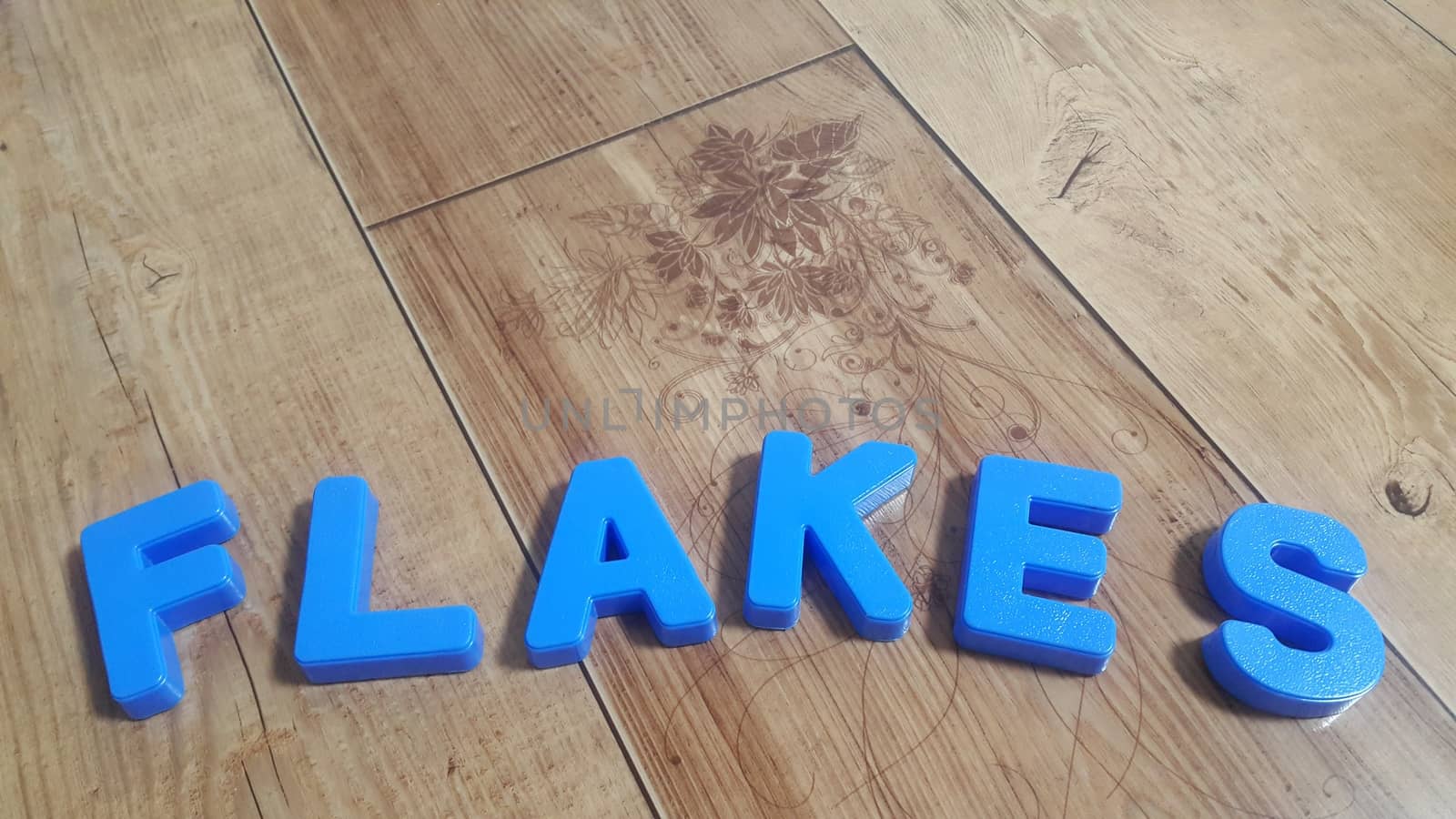 Plastic colored alphabets making words are placed on a wooden floor by Photochowk