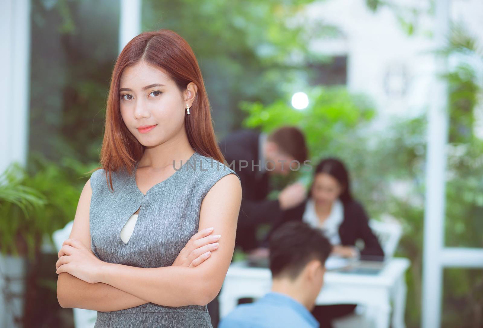 Successful business asian woman standing with with arms folded with her staff at modern office background.