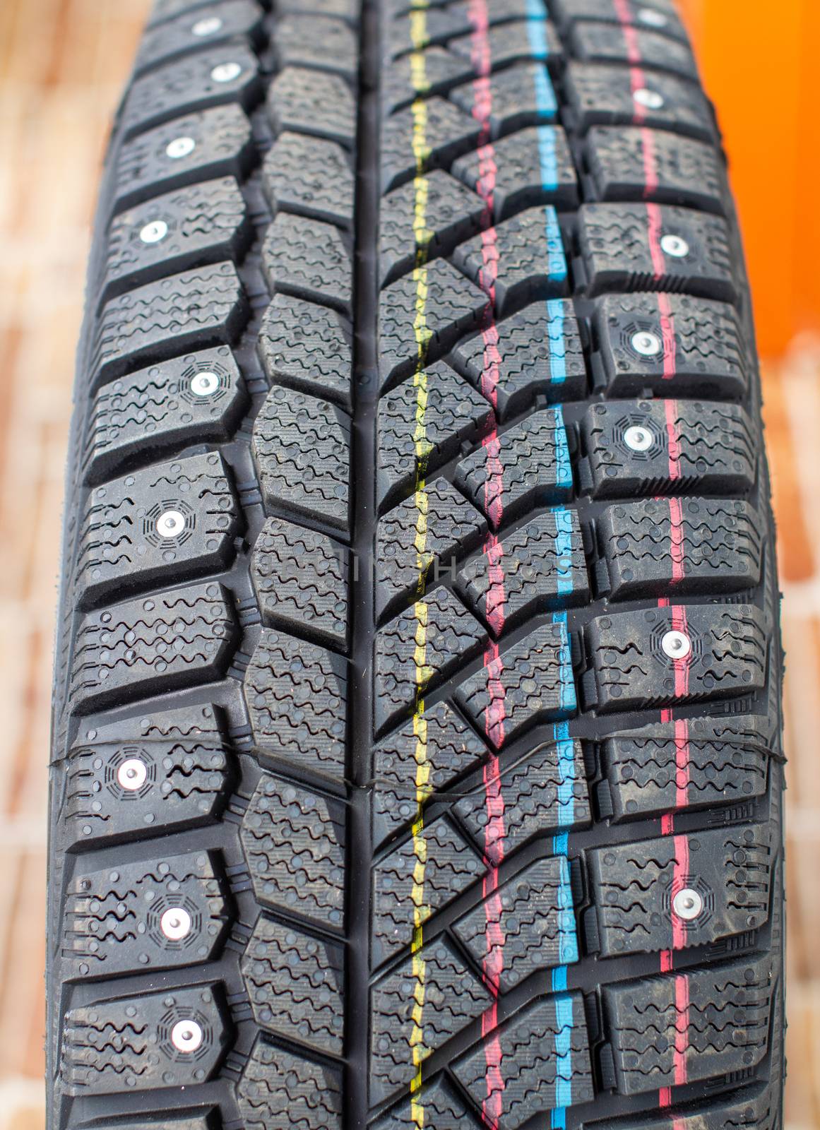 New, black winter car tires with spikes. Safe driving, preparing for winter. Tires with yellow, blue and red stripes