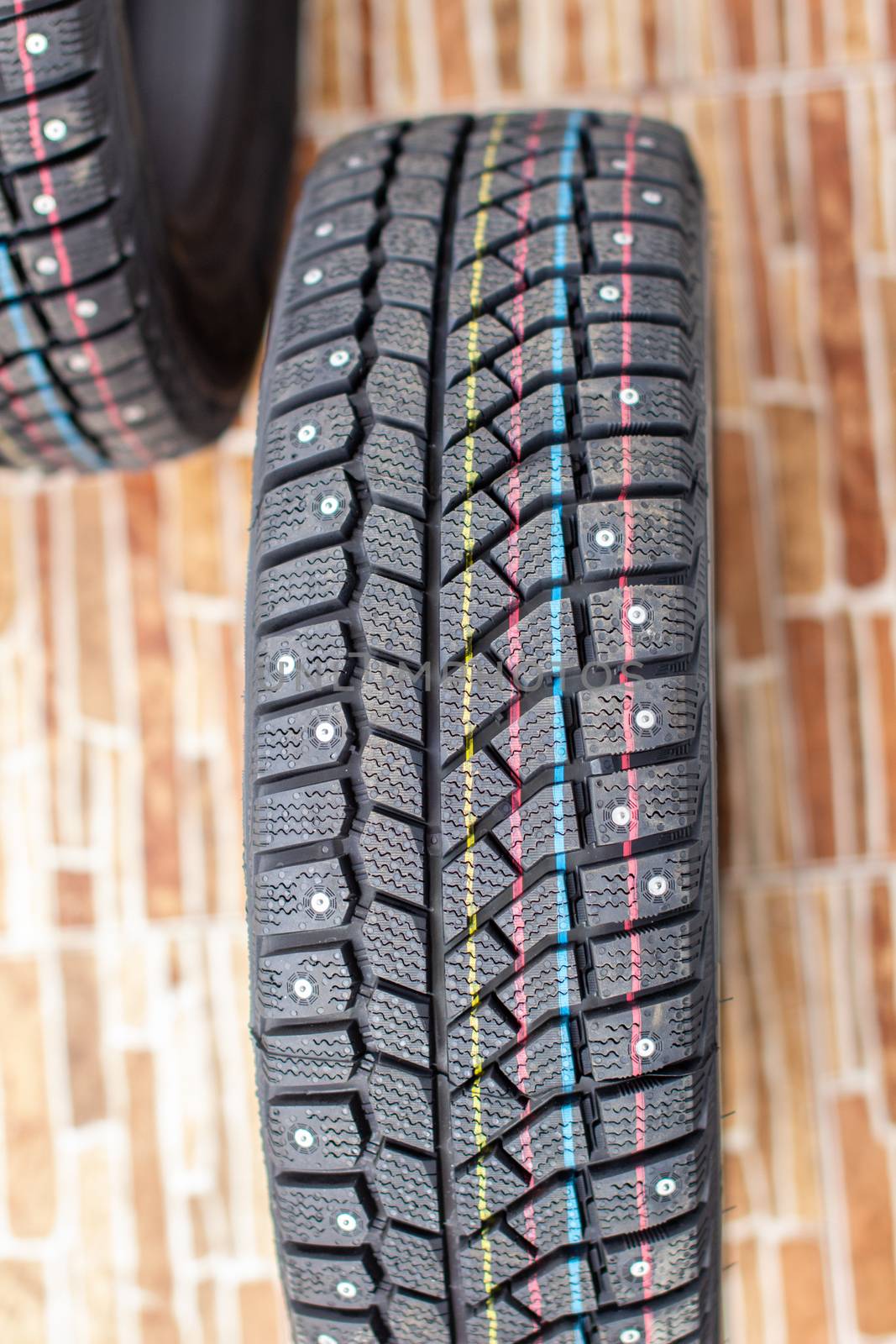 New, black winter car tires with spikes. Safe driving, preparing for winter. Tires with yellow, blue and red stripes