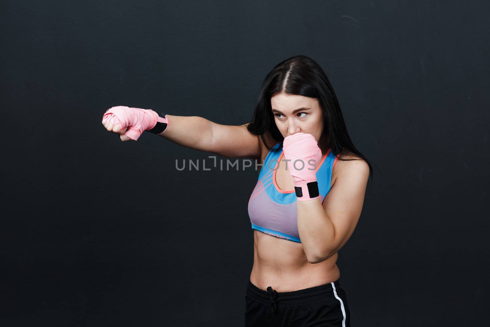 Sportsman woman boxer posing in training studio at black background