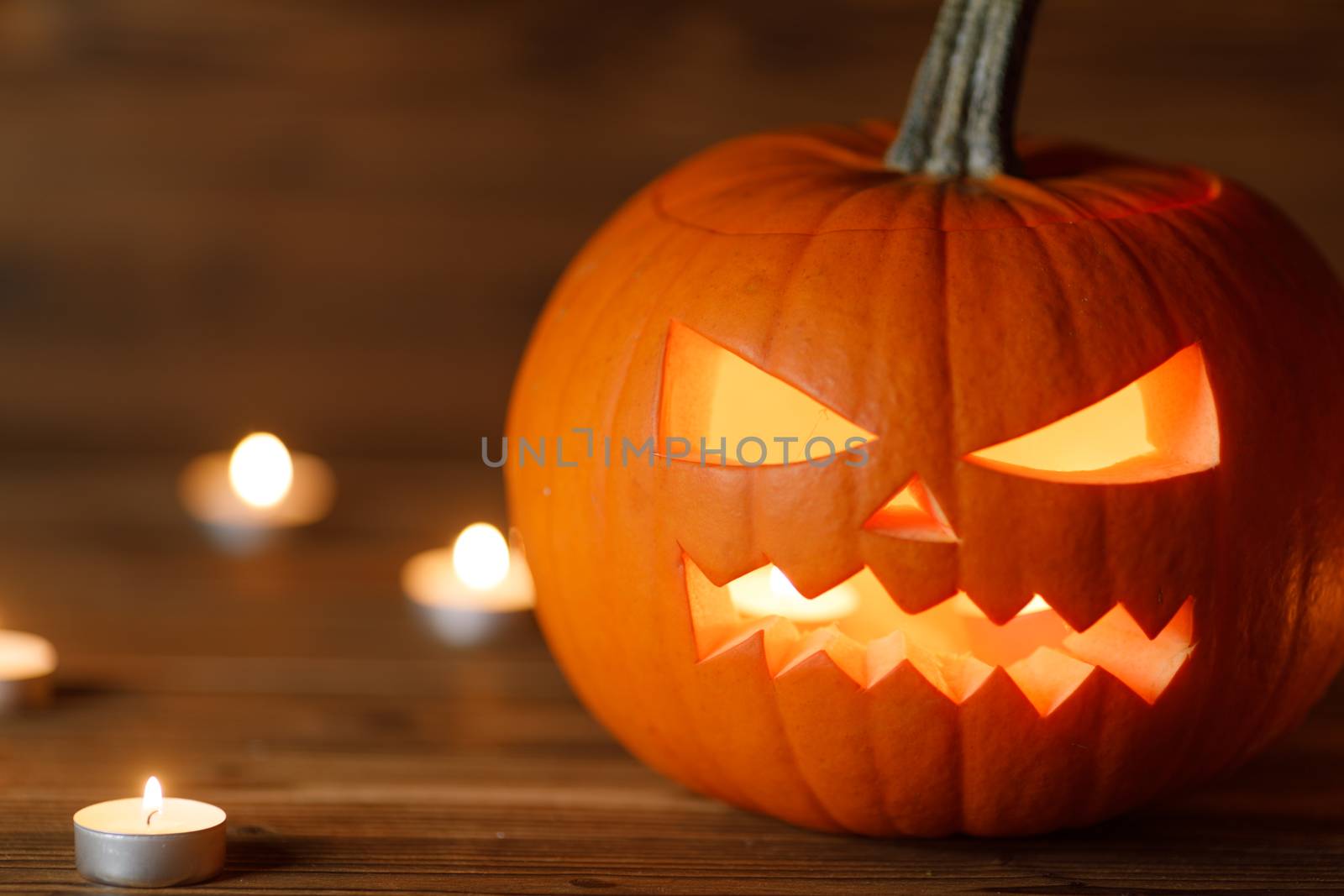 Halloween Jack o Lantern pumpkin head and burning candles on wooden background