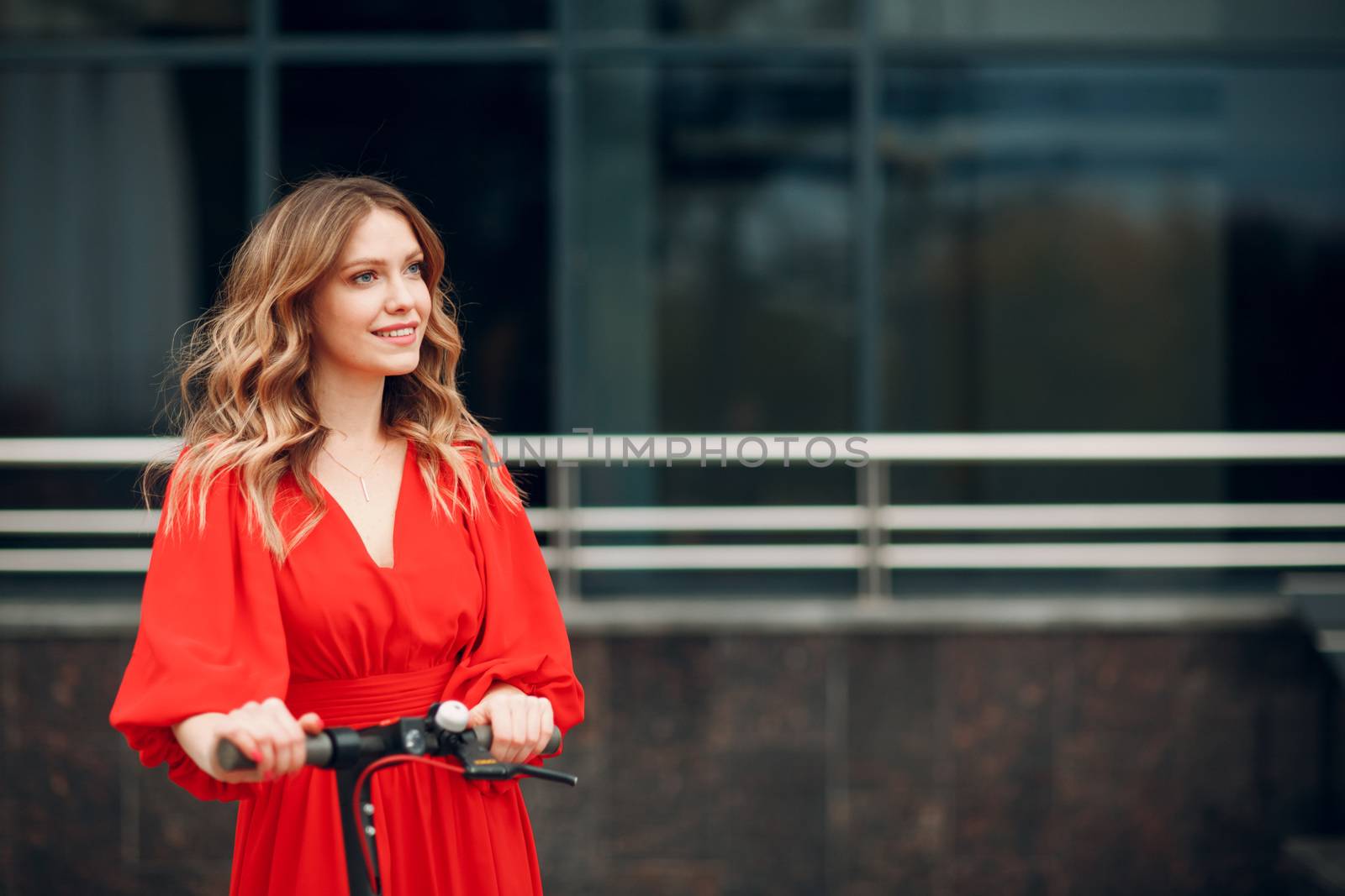 Young woman with electric scooter in red dress at the city by primipil