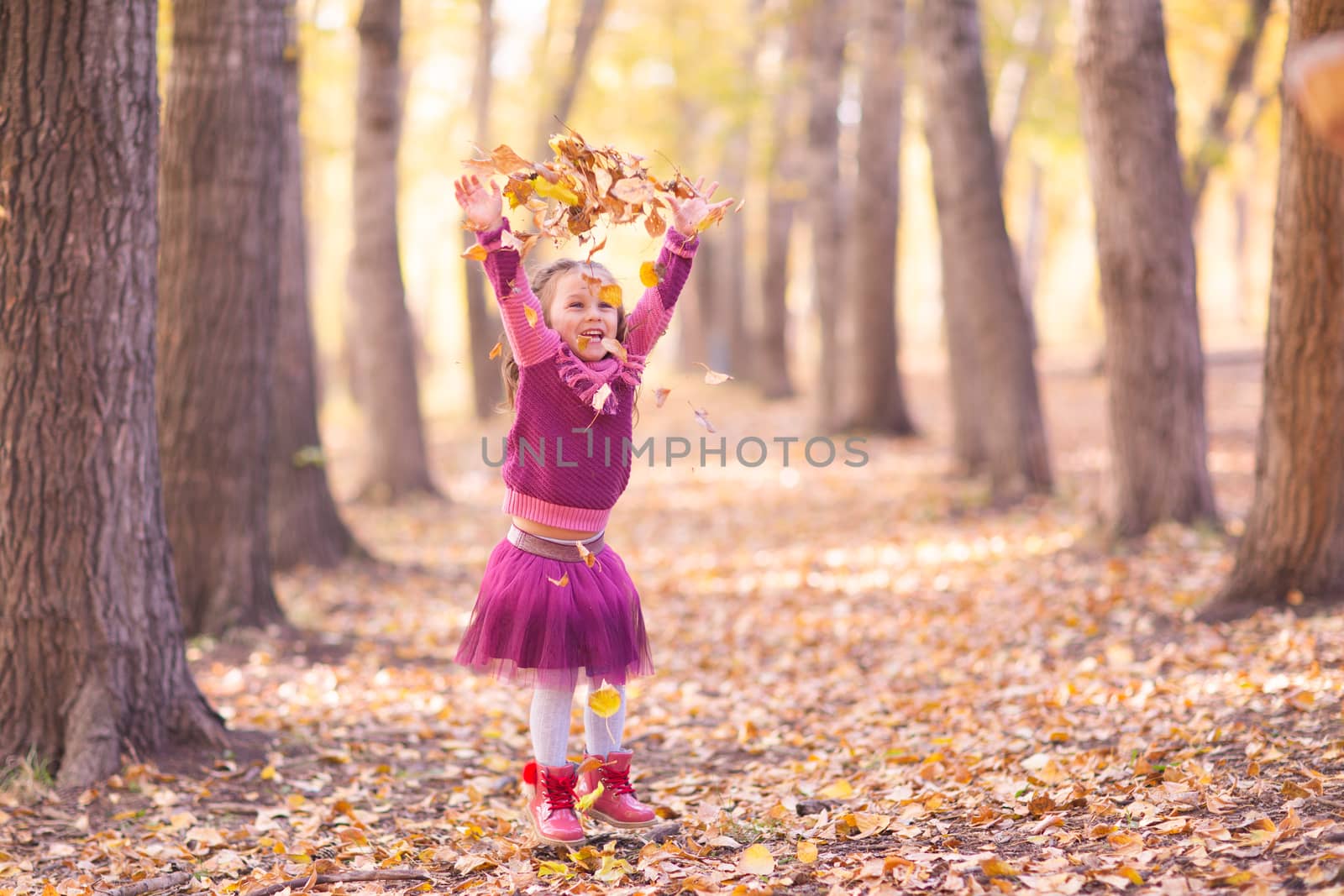 Cute little girl in autumn park with orange and yellow color leaves.