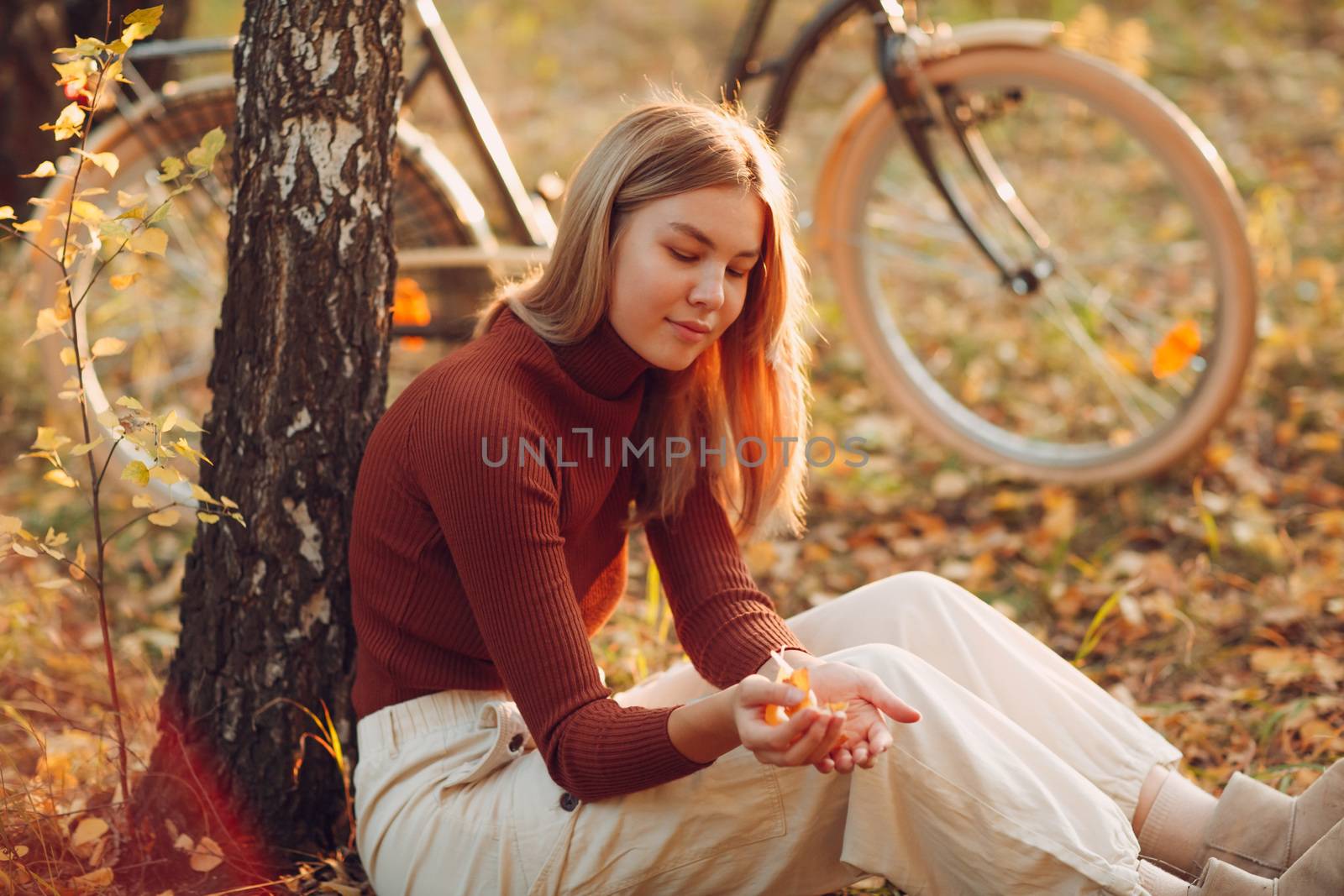 Happy active young woman sitting with vintage bicycle in autumn park at sunset by primipil
