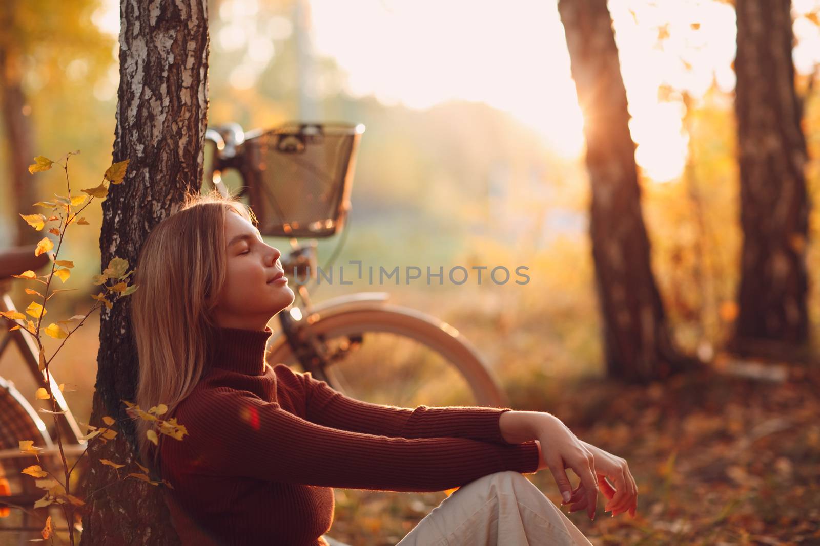 Happy active young woman riding vintage bicycle in autumn park at sunset.