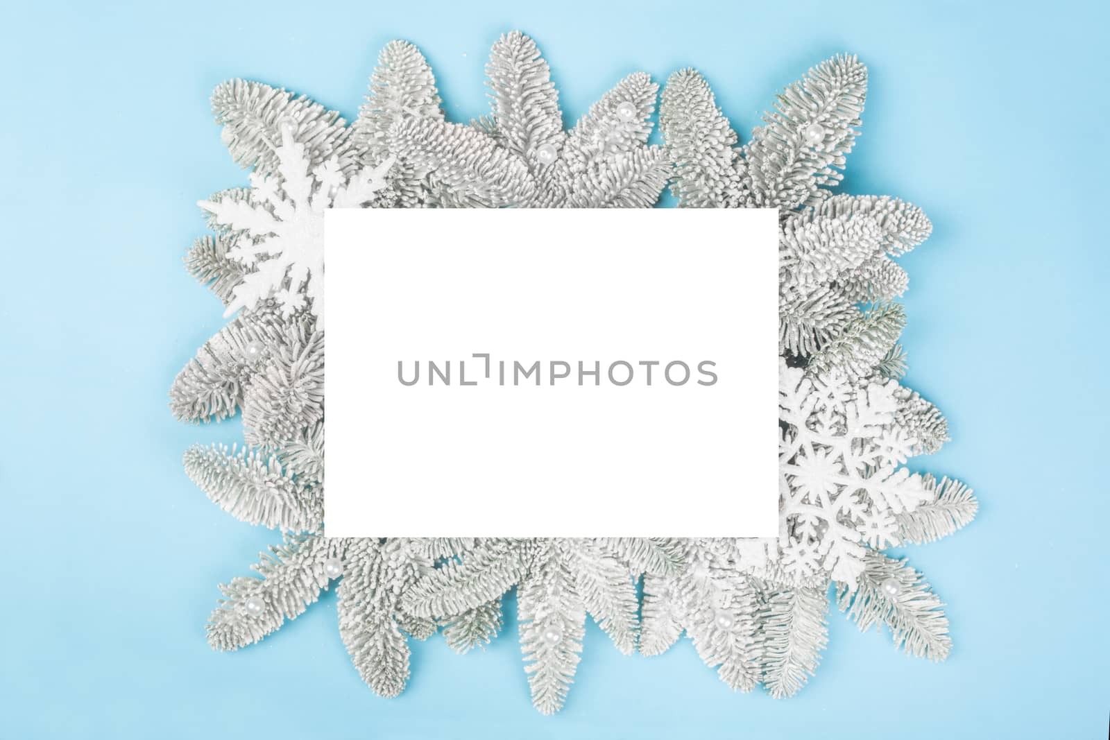 Frosted fir tree twigs and Christmas decorative bauble balls on blue background with white rectangle card with copy space for text template flat lay top view design