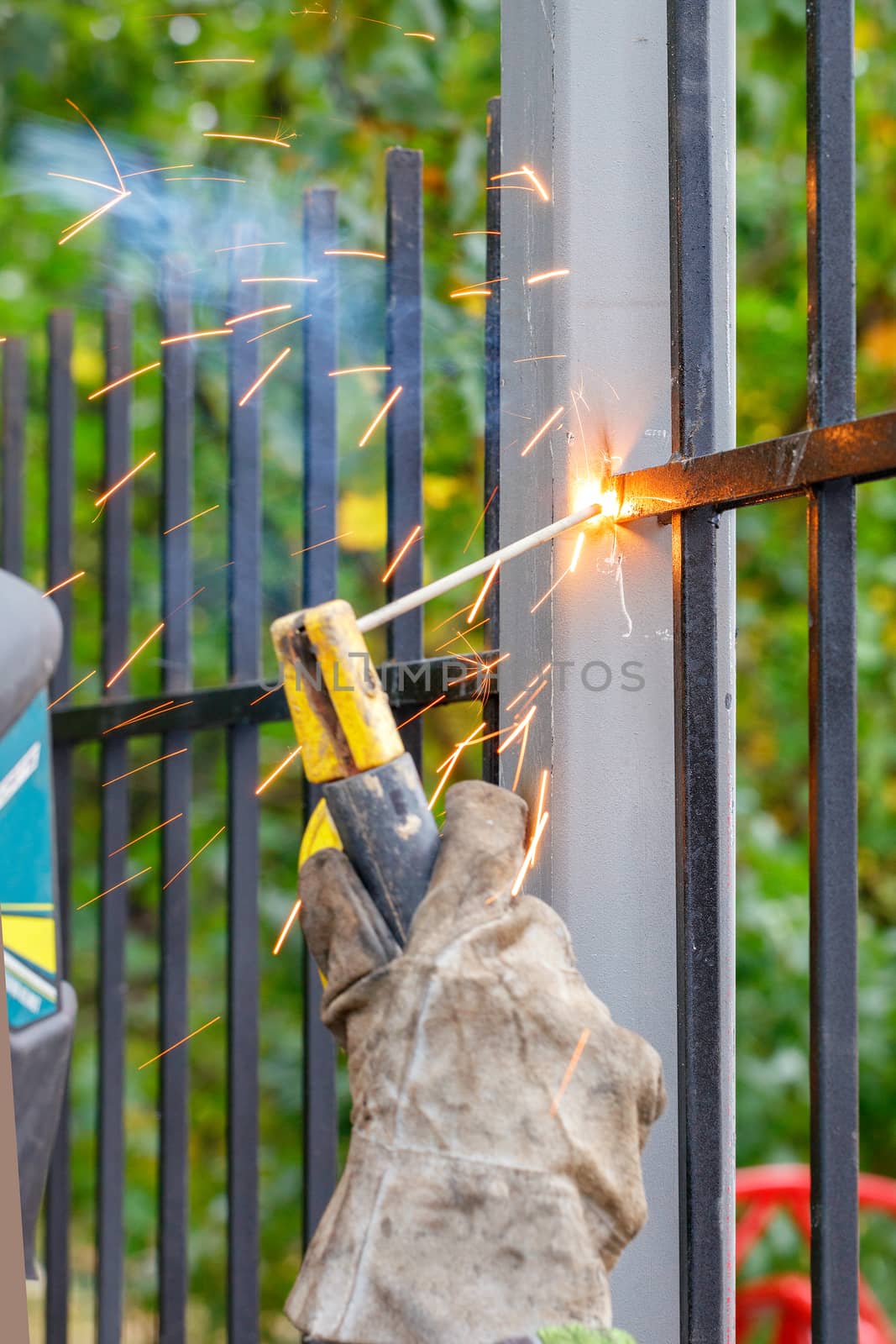 A welder works with metal, welds a metal fence in a park area. by Sergii