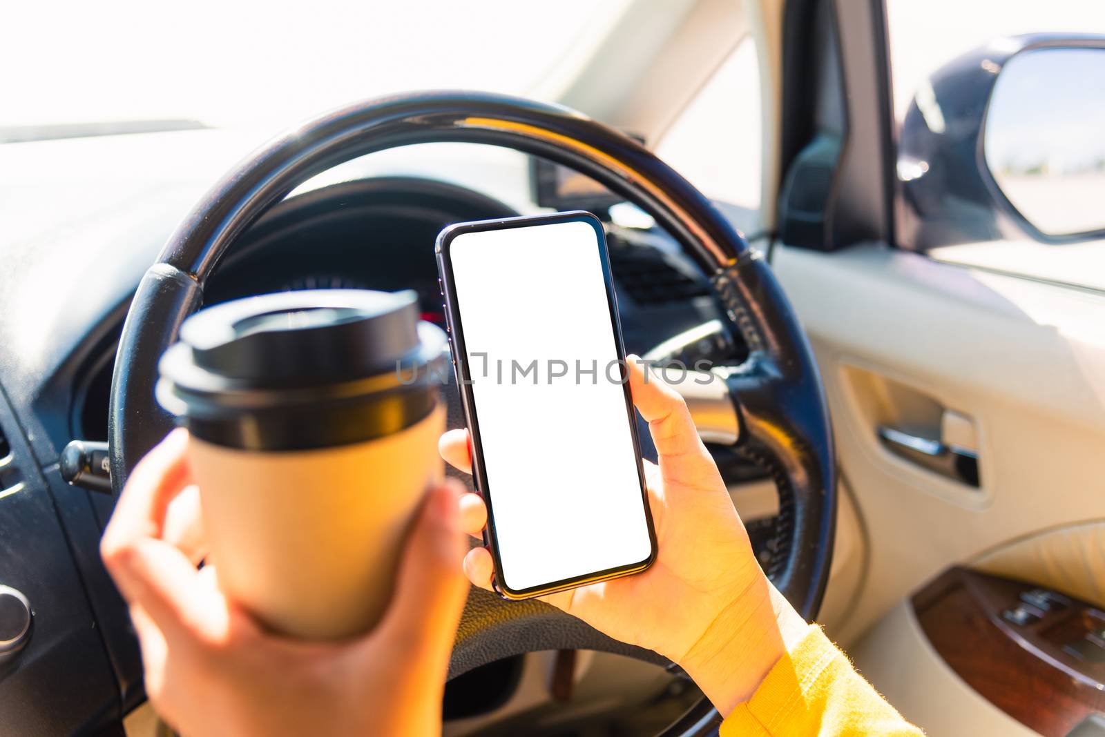 Asian woman drinking hot coffee takeaway cup inside a car and using smartphone blank screen while driving the car in the morning during going to work on highway, Transportation and vehicle concept