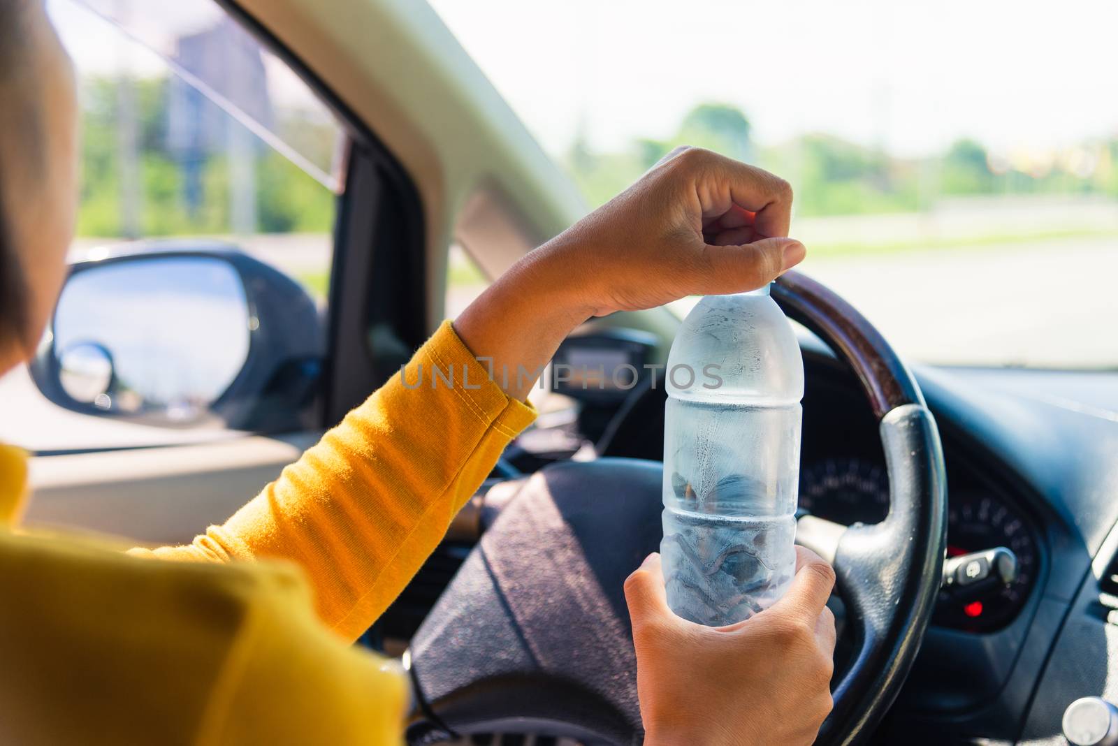 woman holding a water bottle for drink while driving the car by Sorapop