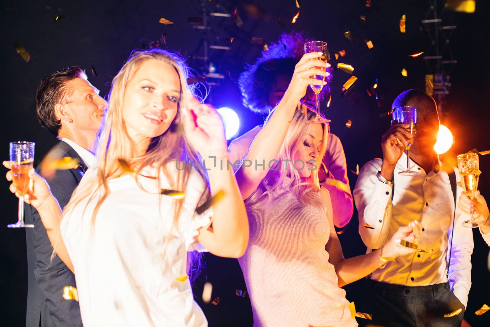 Having fun together. Group of beautiful young happy multi race people dance holding champagne in golden confetti and smiling nightlife new year celebration party