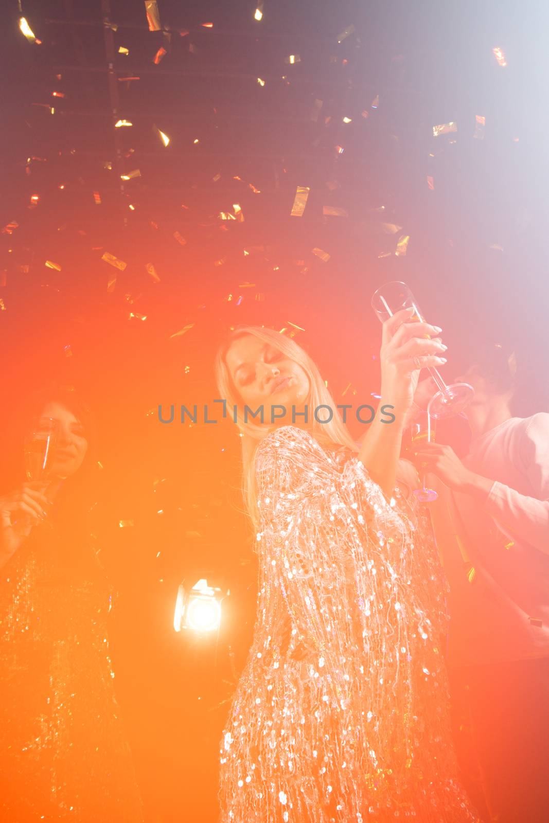 People having fun at 80s retro style party. People wearing costumes drinking champagne and dancing on dancefloor at nightclub in golden confetti