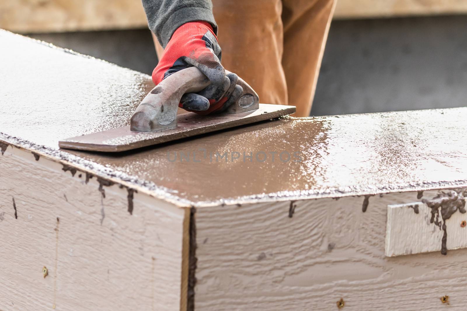 Construction Worker Using Wood Trowel On Wet Cement Forming Coping Around New Pool.