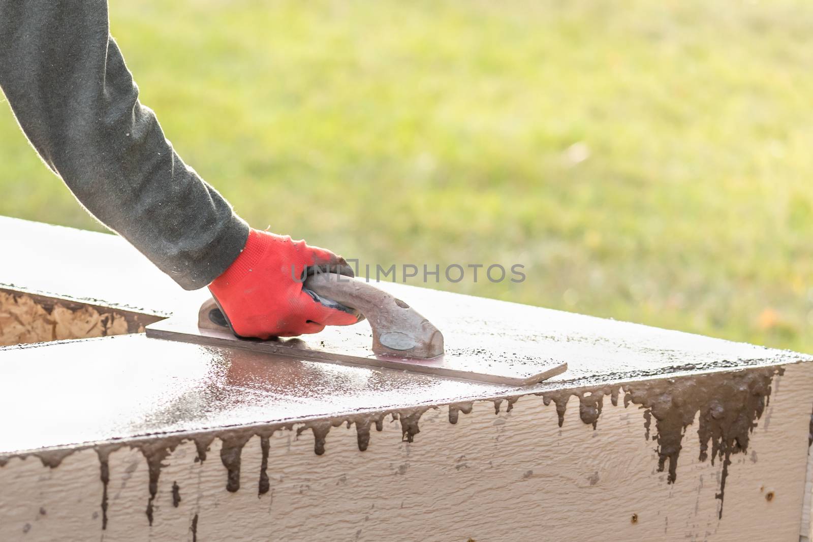 Construction Worker Using Wood Trowel On Wet Cement Forming Coping Around New Pool.